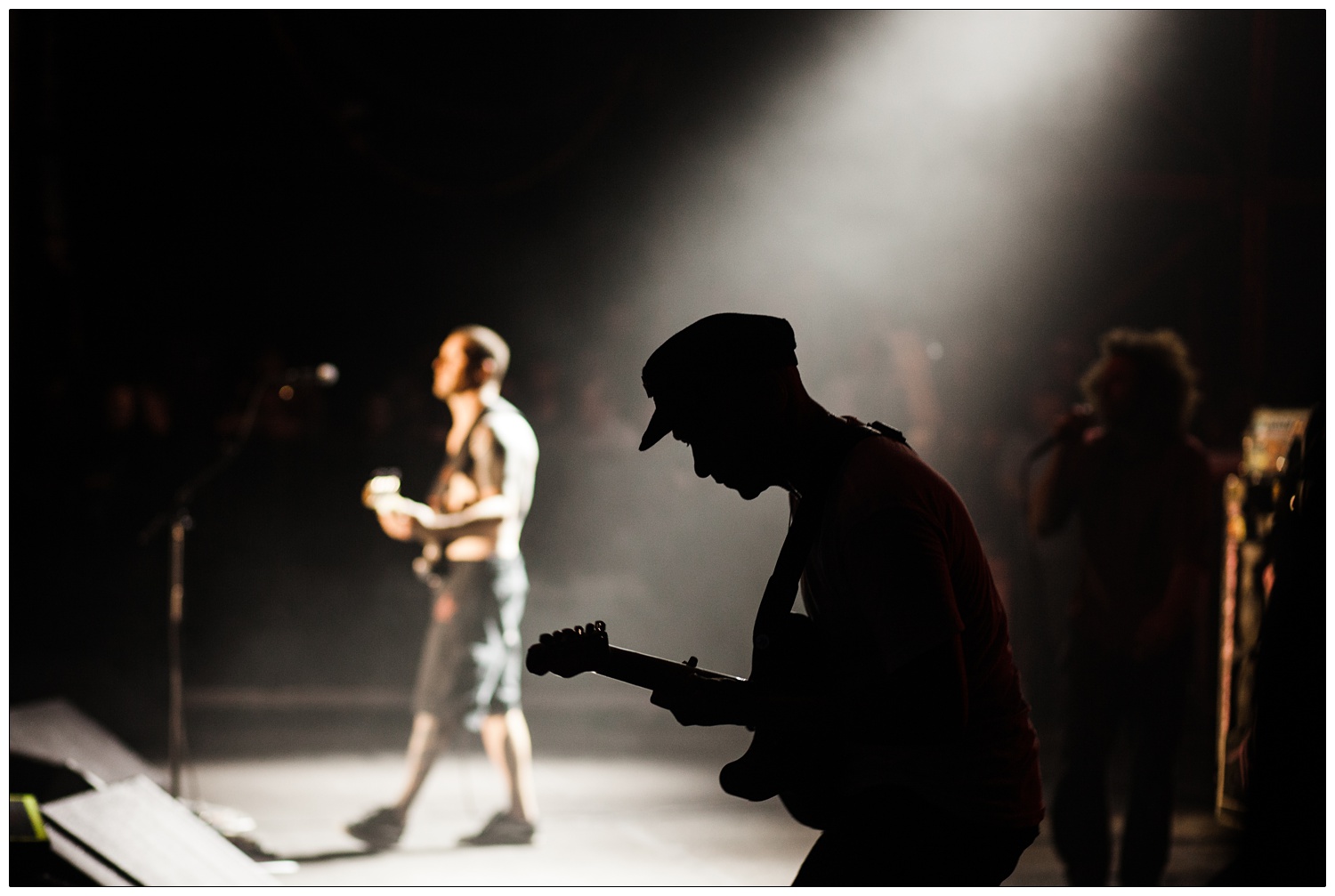 Silhouette of Tom Morello playing in 2010, Tim Commerford and Zack de la Rocha in the background.
