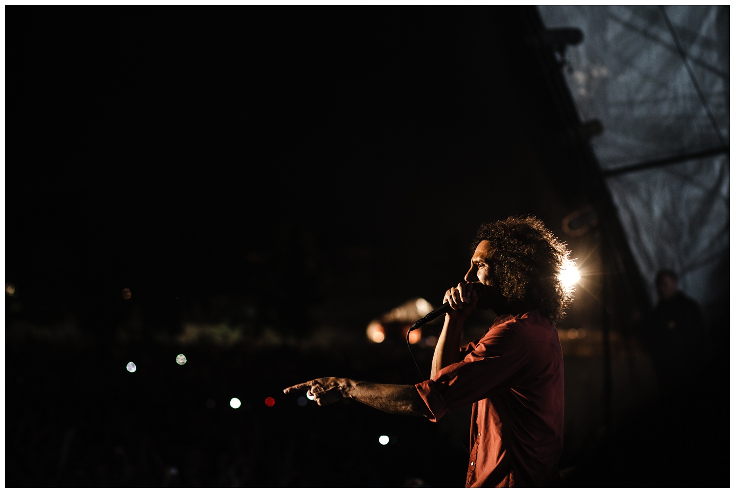 Zack de la Rocha performing on stage in Finsbury Park 2010. He is pointing out to the crowd and a light shines behind him