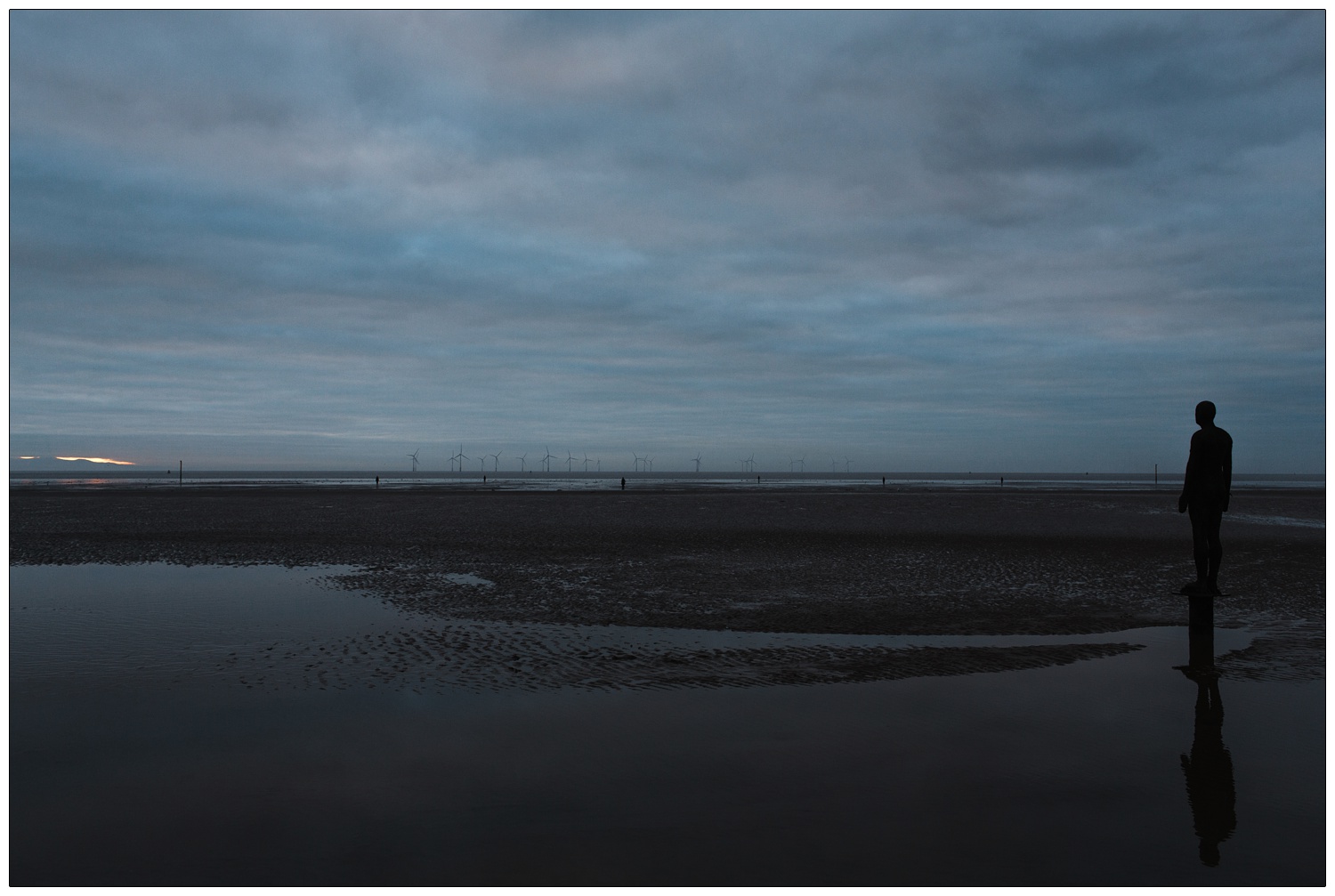 Cast iron sculptures on beach, wind turbines in the distance Antony Gormley Another Place Crosby Beach Liverpool