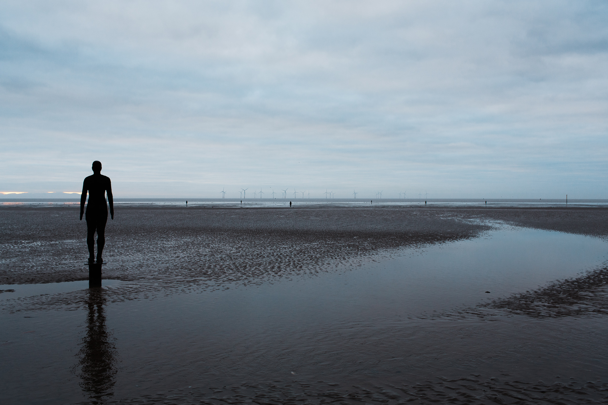 Crosby beach showing Antony Gormley's Another Place cast iron figures and a wind farm