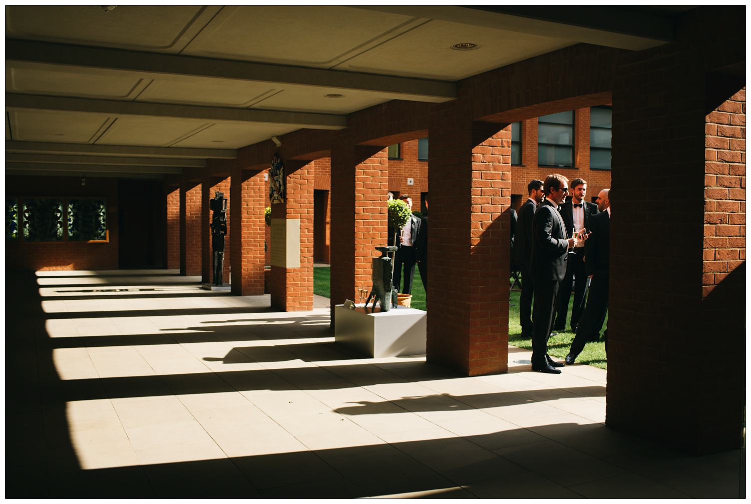 Haberdashers' Hall in Smithfield, shadows are cast on a walkway. Men having drinks in the courtyard.