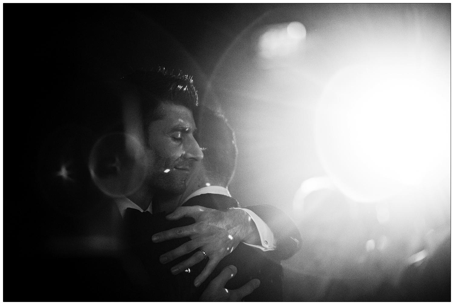 The grooms hugging each other during the first dance. The light is flaring behind them.