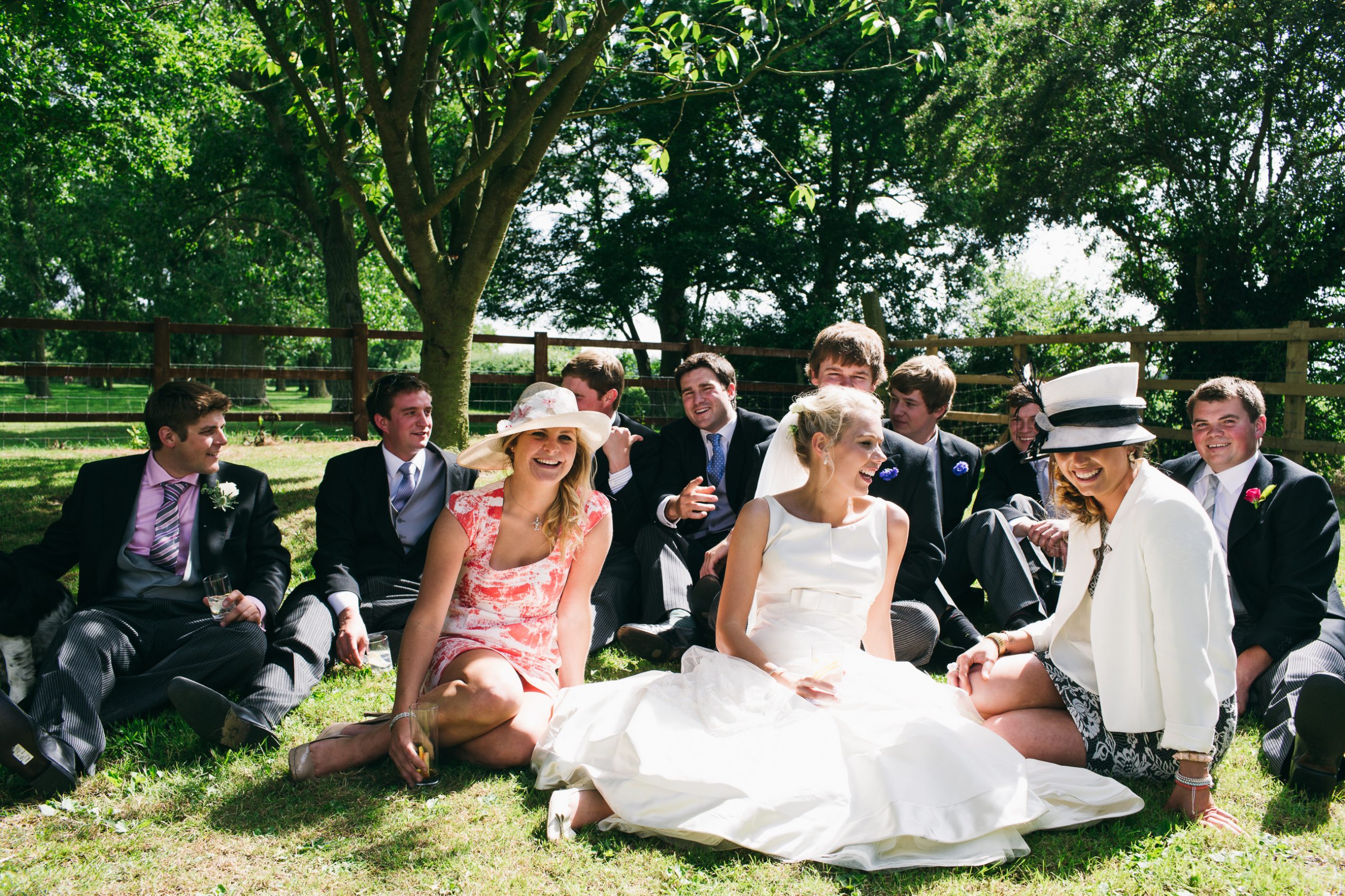 Bride with her friends sat down on the lawn in the sunshine. A wedding in Essex on a farm.