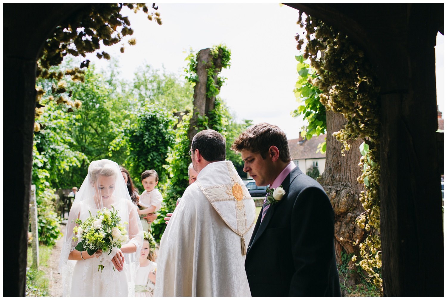 Bride looking down before her ceremony. The vicar is in the door way.