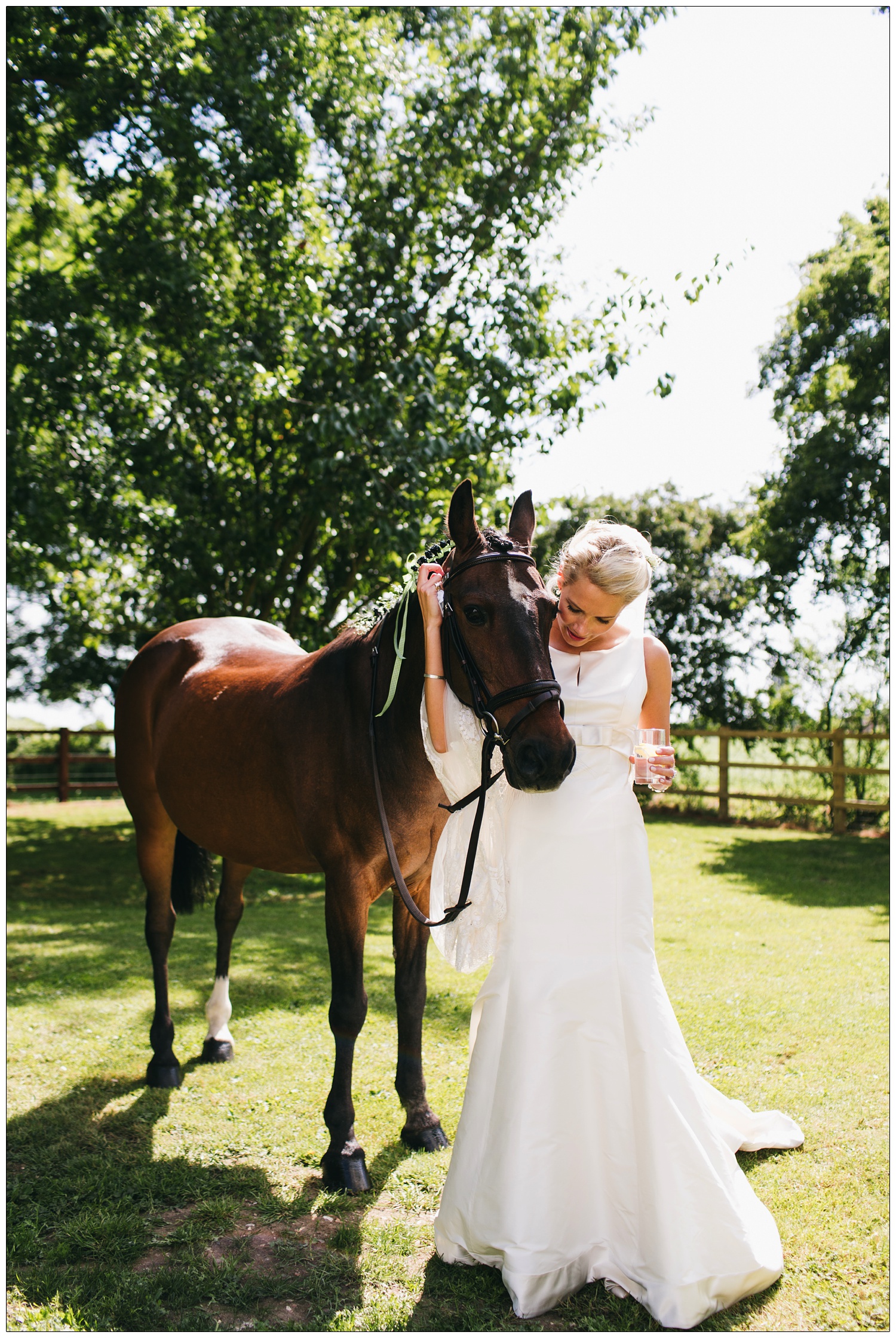 A bride hugs her horse while holding a drink.