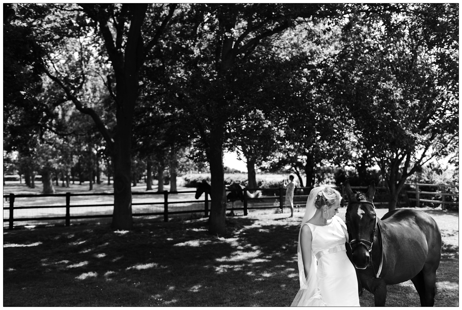A woman in a wedding dress with her horse. There are trees behind them and dappled light.