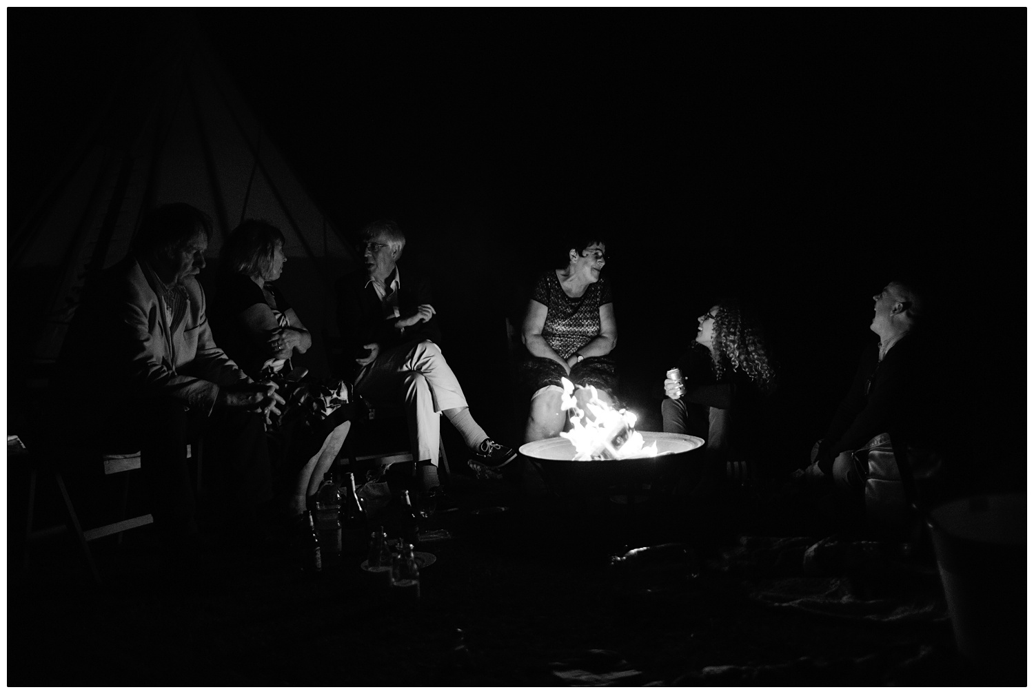 Family and friends at a wedding gather around a fire pit at night.