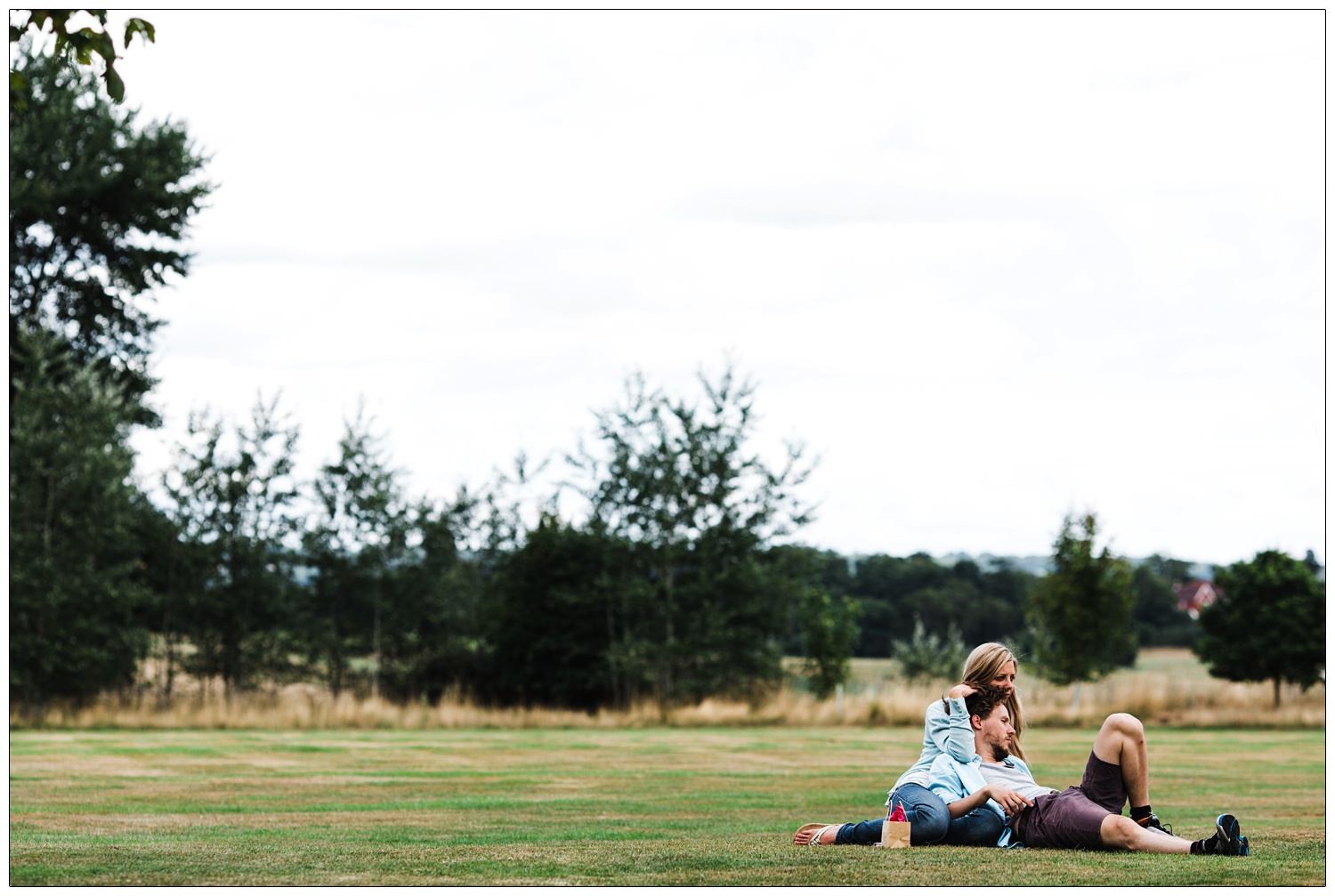 A couple who were guests at the wedding the day before are sitting and laying on the grass.