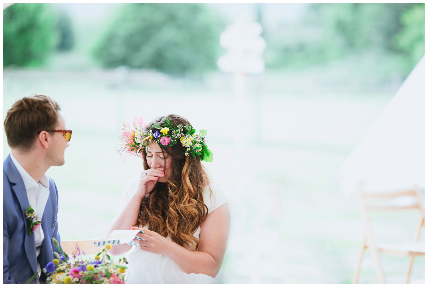 The bride is emotional during the speeches. Her groom is looking at her, he still has his sunglasses on.