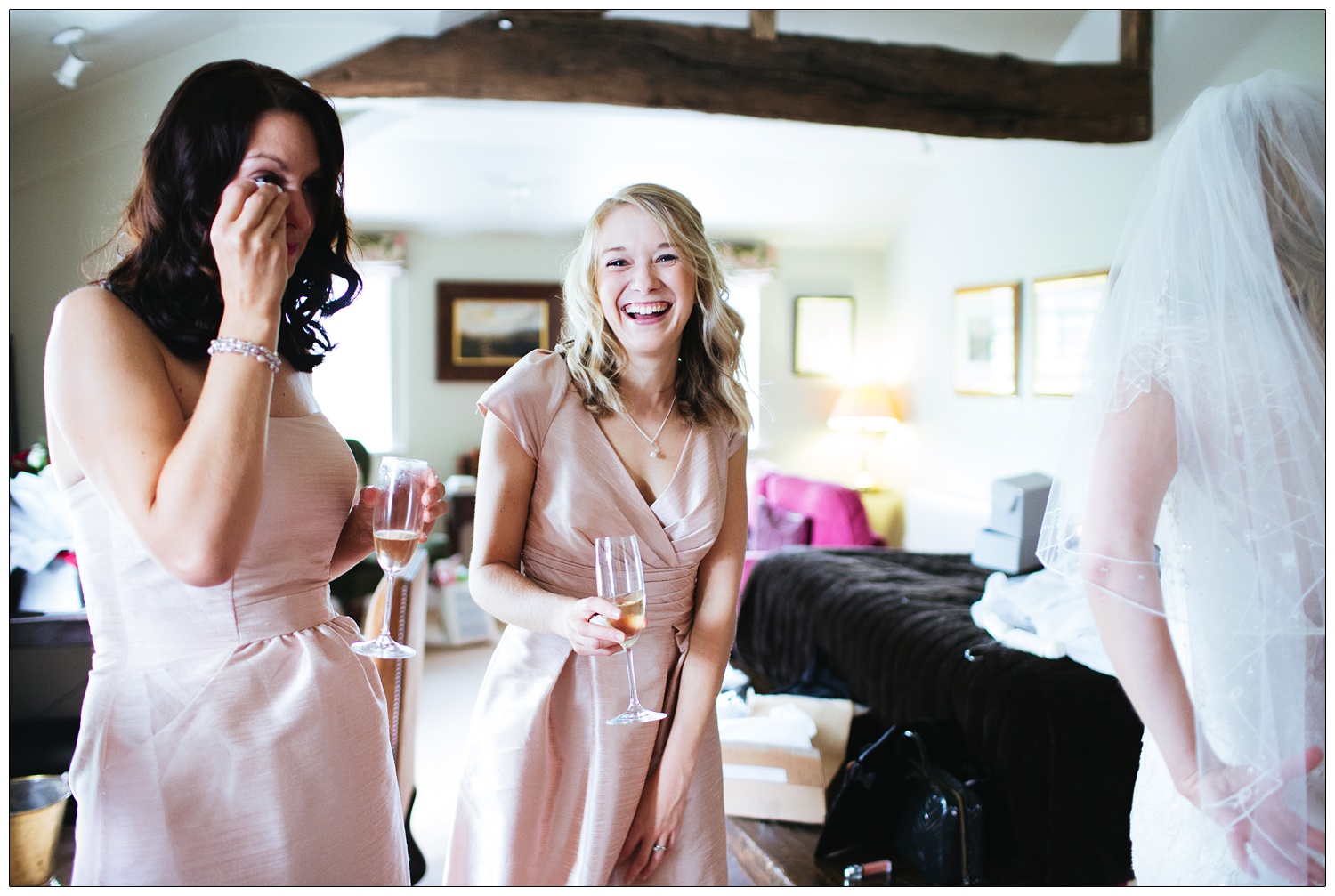 Bridesmaid is laughing at the camera, she's wearing pink and holding a glass of prosecco.