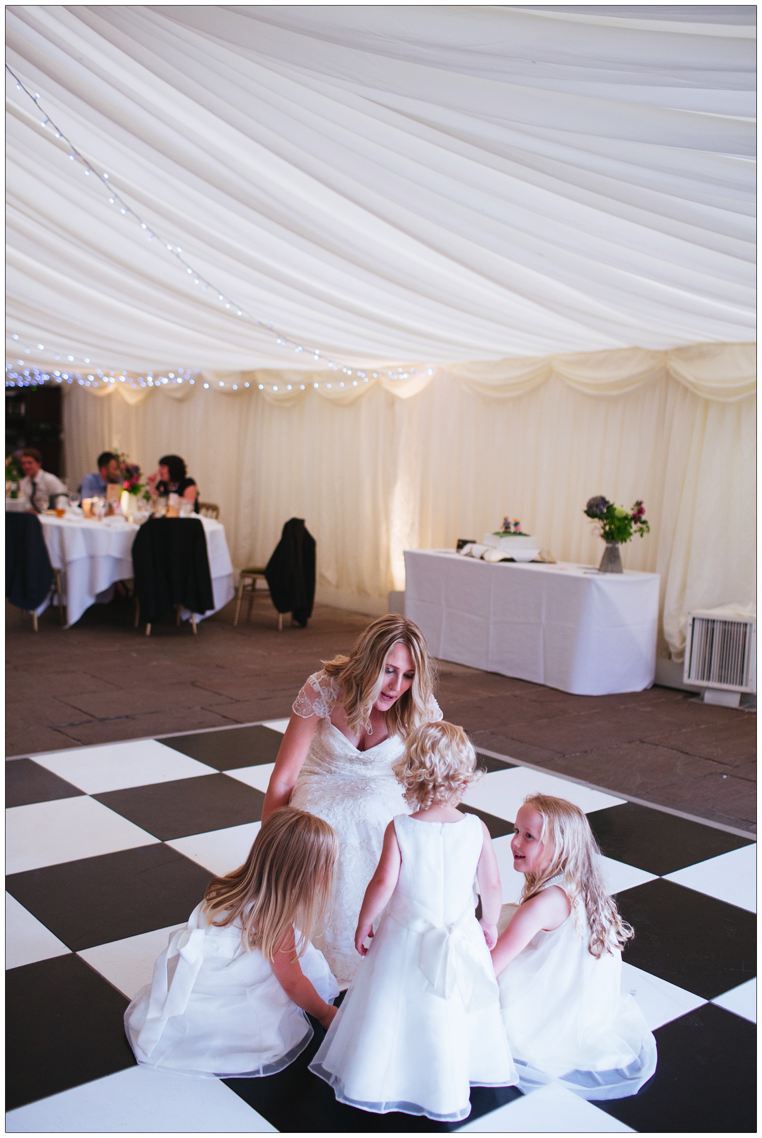 A woman on her wedding day is dancing with three small flower girls on a black and white dance floor.