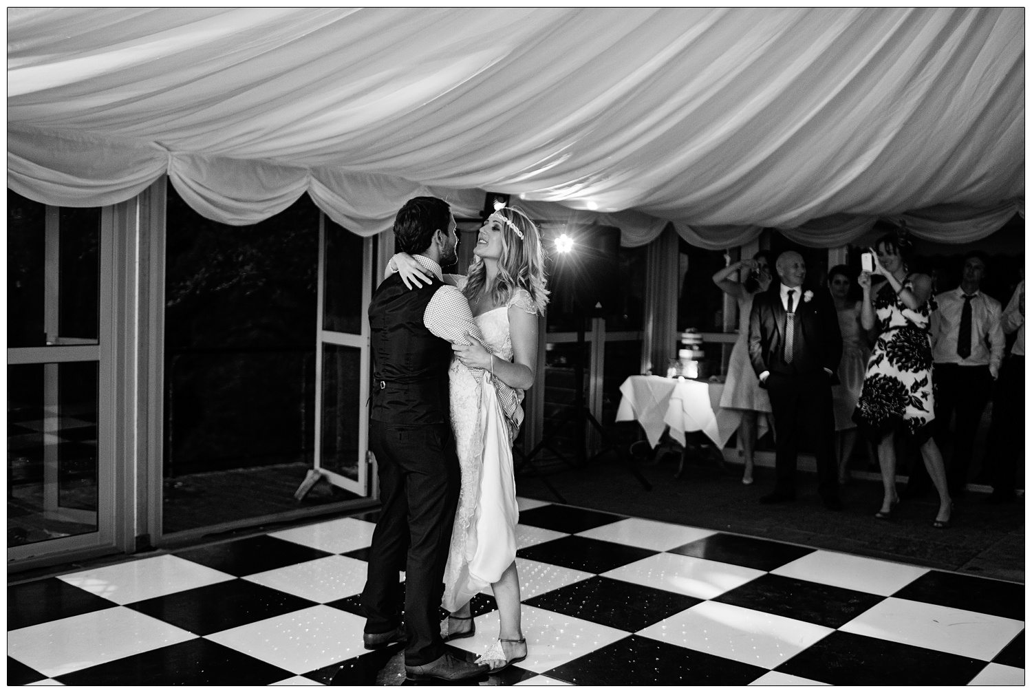 Bride and groom on the black and white chequered floor of a marquee. They are at the Inn at Whitewell having their first dance.