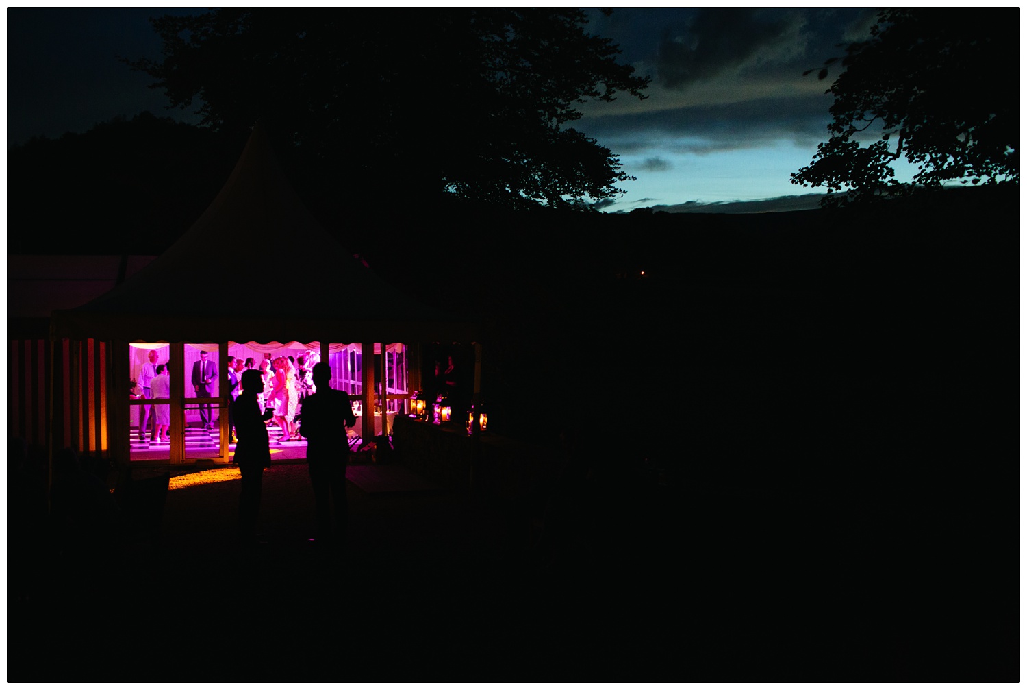 The view of the marquee at the Inn at Whitewell at twilight. The marquee is lit up magenta.