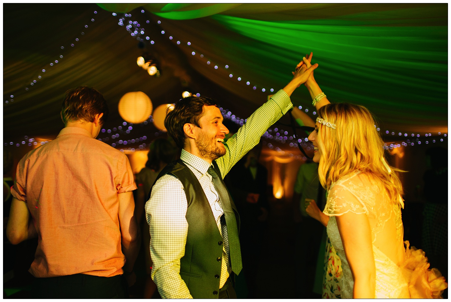 In a marquee a couple who just got married are dancing under coloured lights. Green and orange.