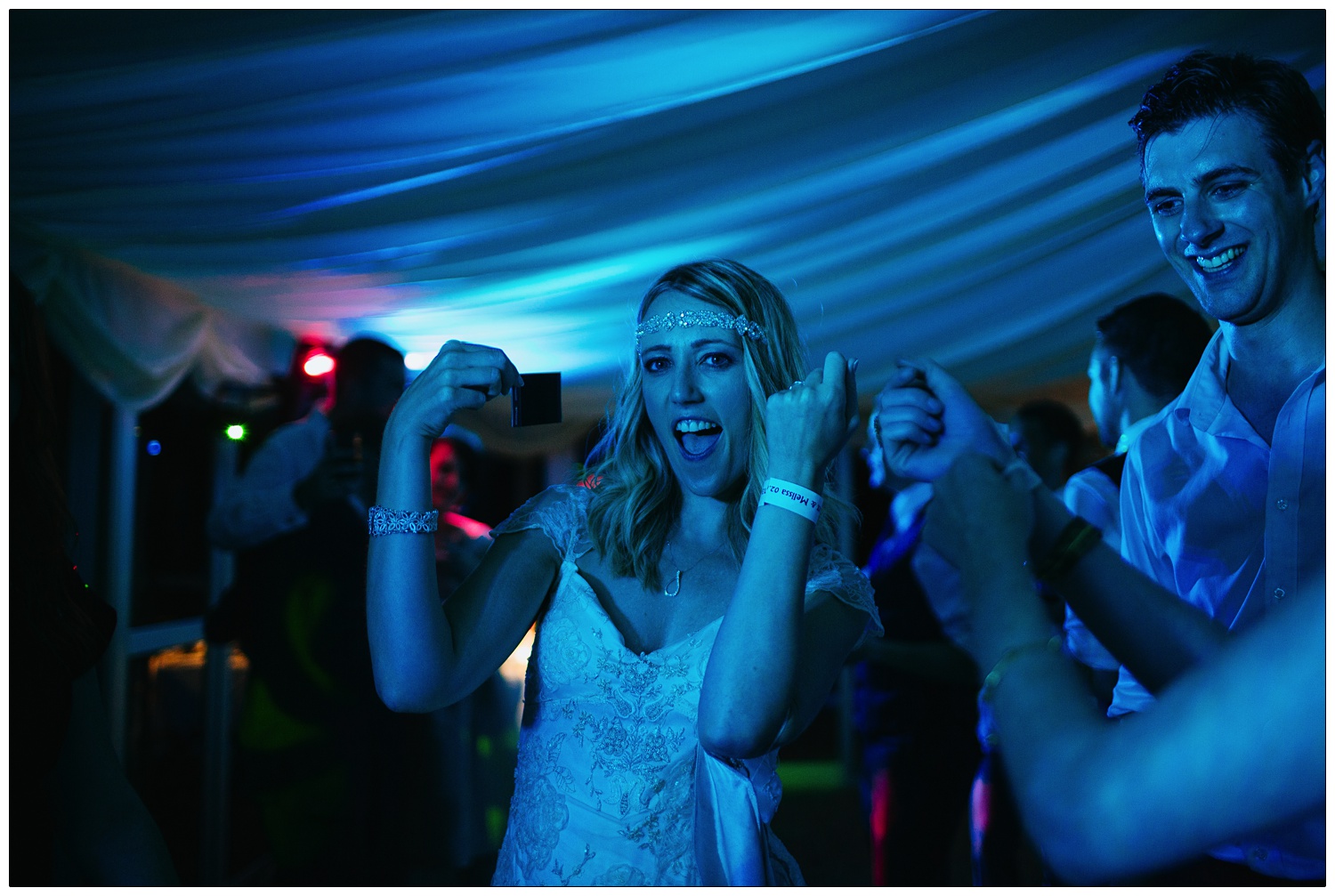 Bride is dancing to Hey Ya! by Outkast, so she is shaking a polaroid picture. The lights are blue in the marquee at The Inn at Whitewell.