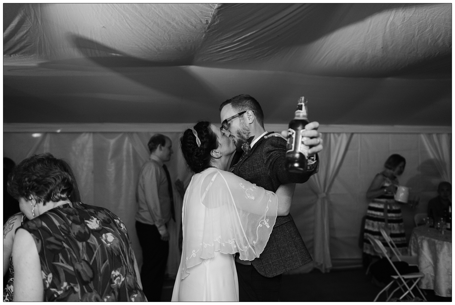 On the dance floor the bride kisses the groom as he holds out his bottle of Tangle Foot beer.