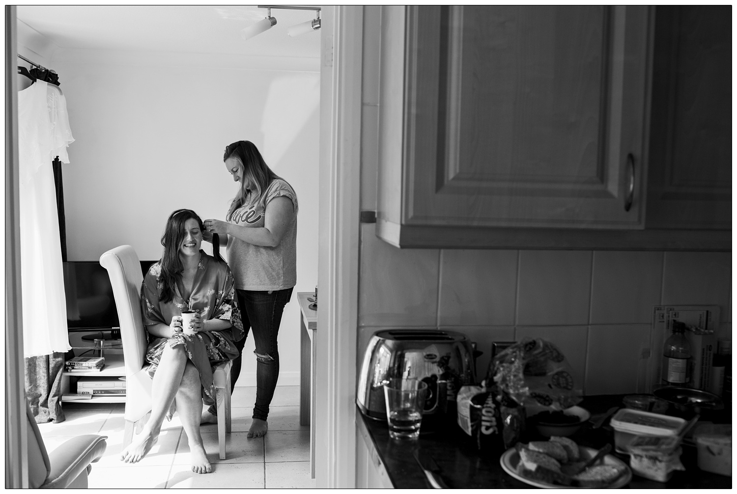 A friend plating the bride's hair. Seen through the doorway from the kitchen.