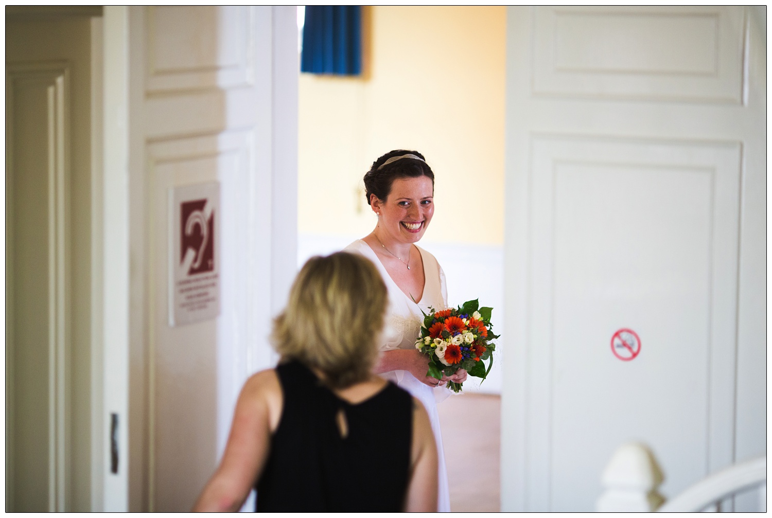 Bride looks excited through a gap in the door as she meets the registrars before the wedding.