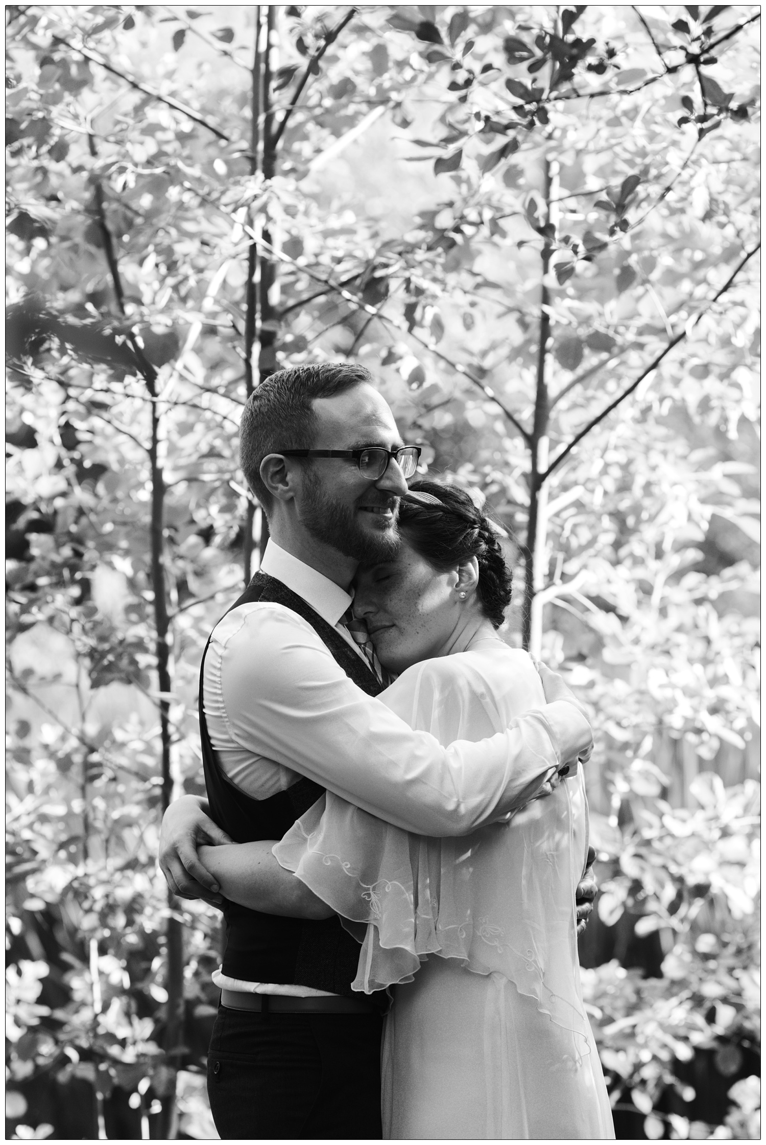 A couple hug in dappled light by trees on their wedding day in Kent.