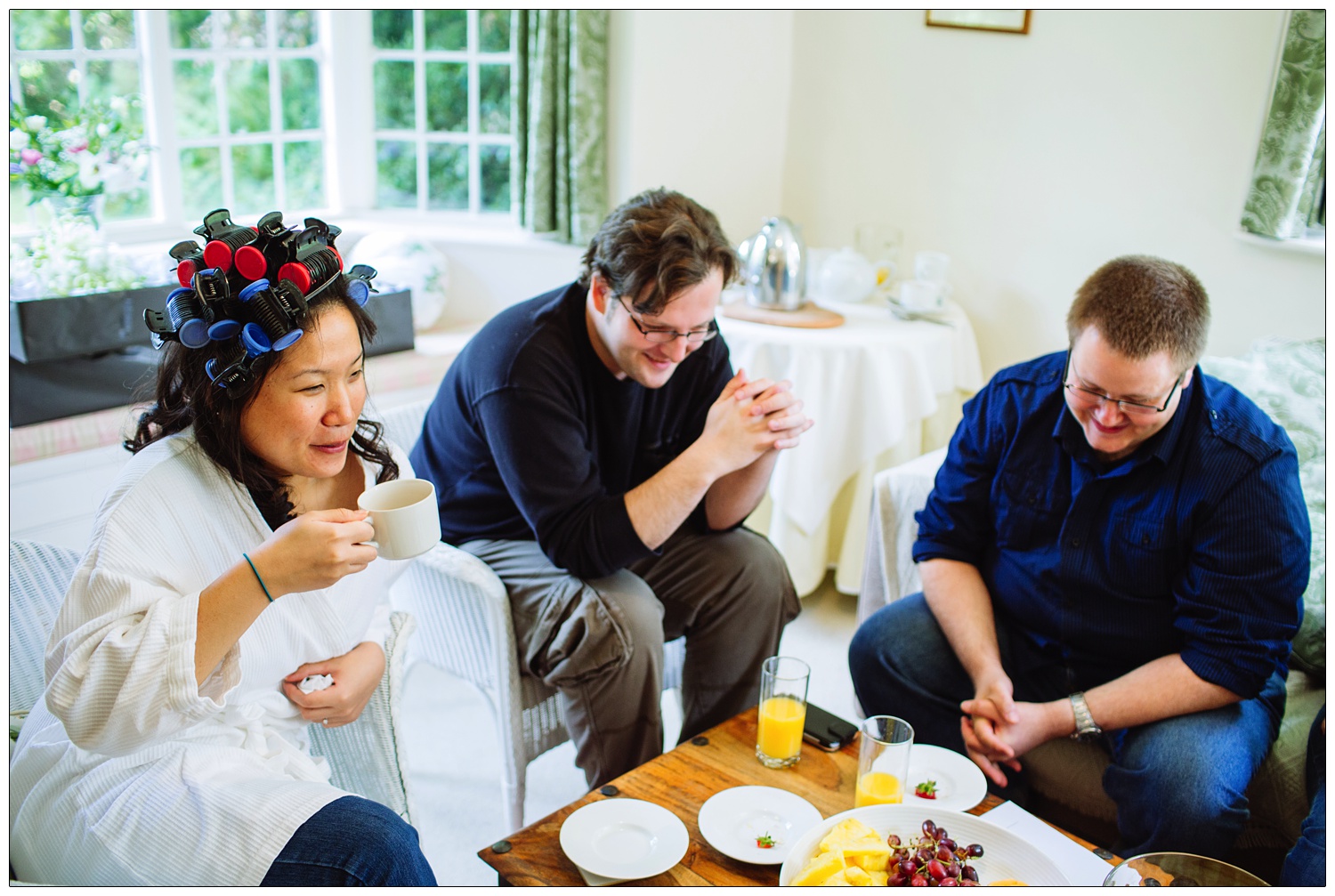 A woman in rollers drinking tea with friends. They are in the living room of the Hedingham castle garden cottage.