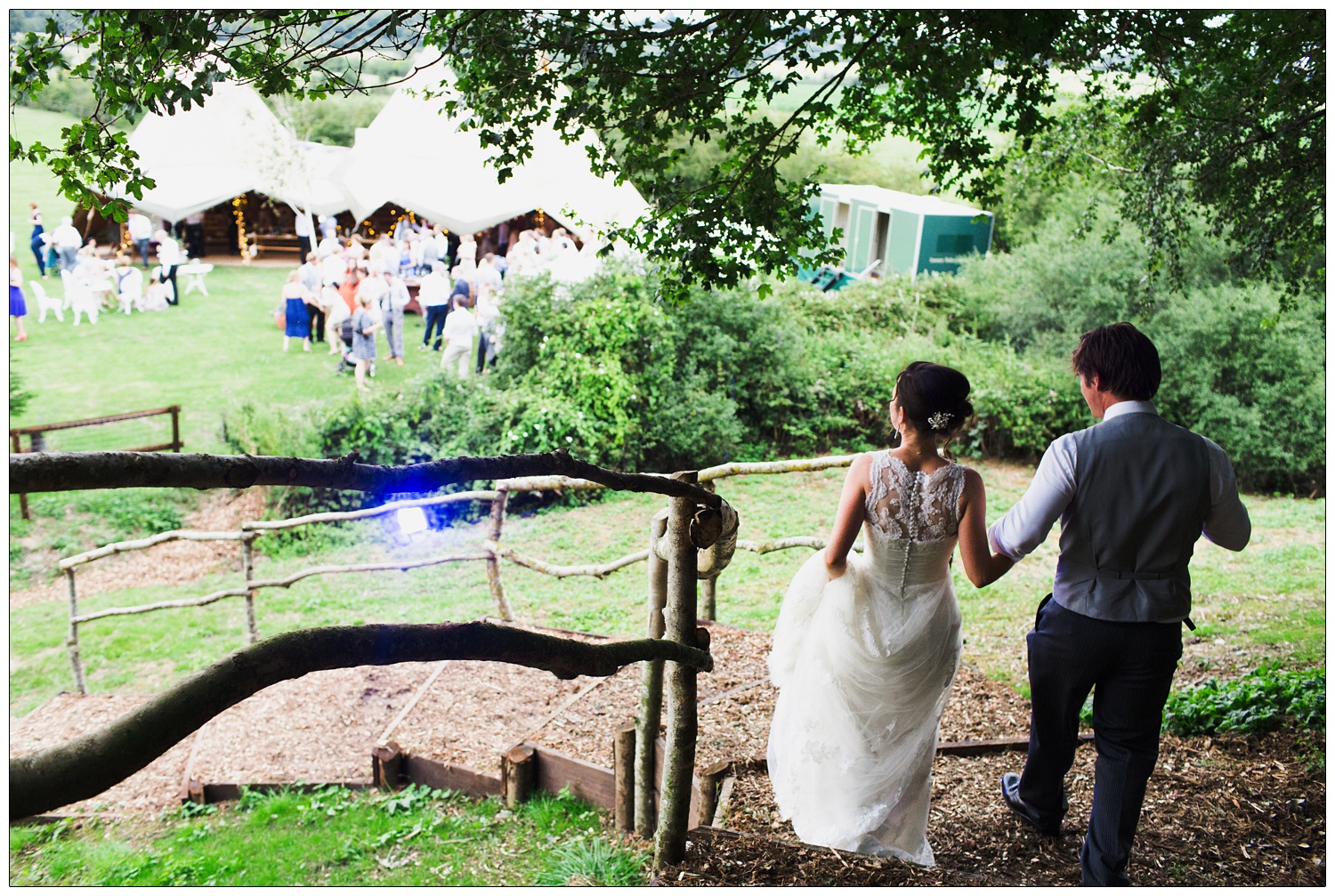 The bride and groom walk down the wooden steps to the Tentipi, for their wedding reception. The guests are already down there.