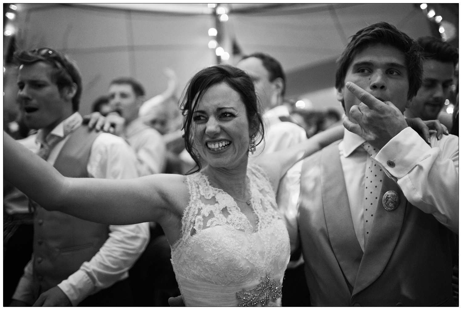 The groom is wolf whistling and his wife is smiling as they dance on packed dance floor at a wedding in Essex.