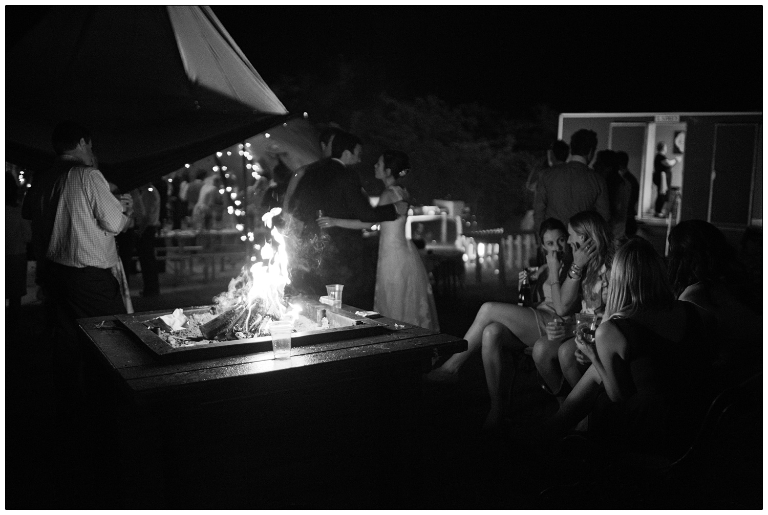 Women sit around a fire pit. A bride is talking to two people in the background.