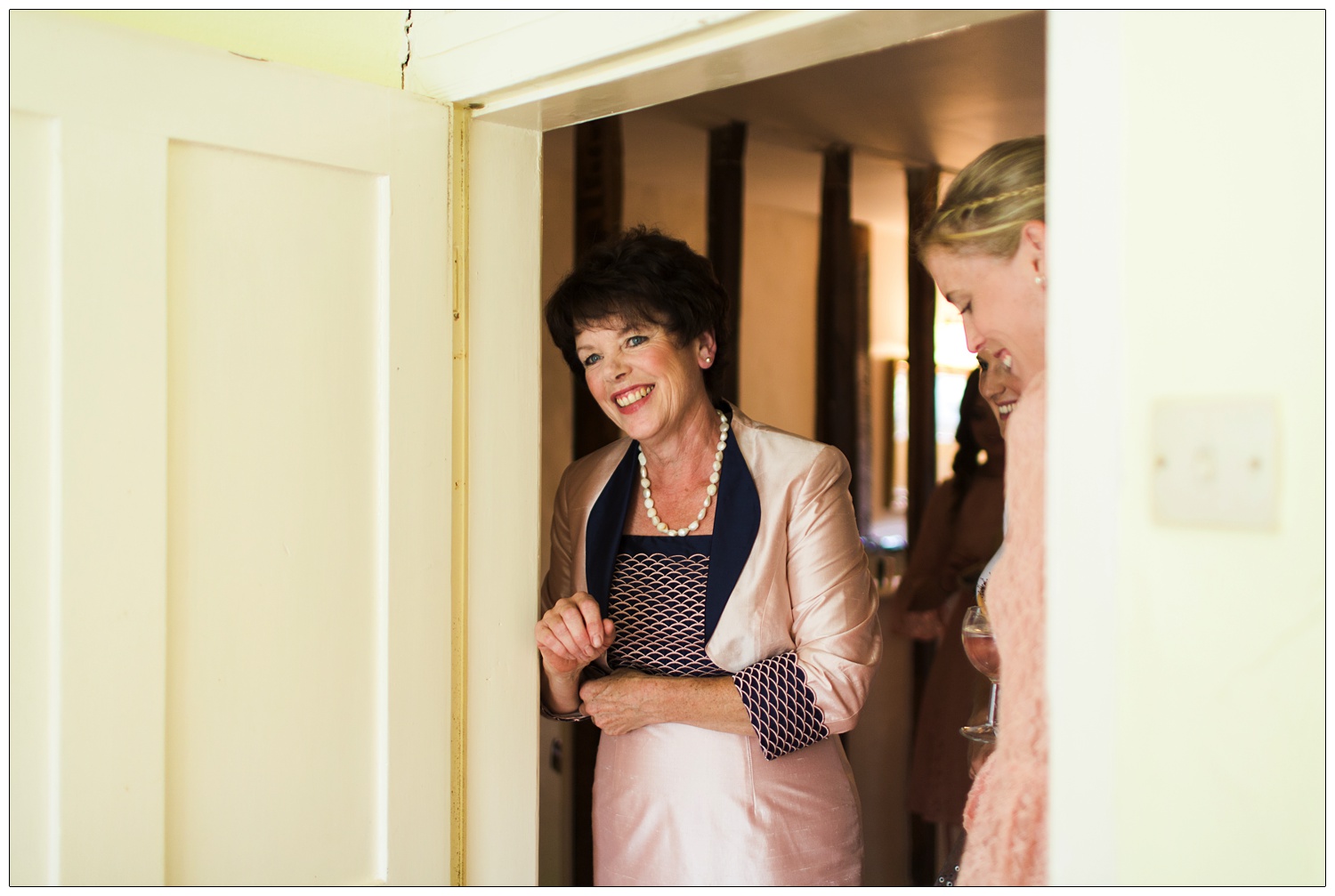 Mother of the bride stands in a doorway and smiles.