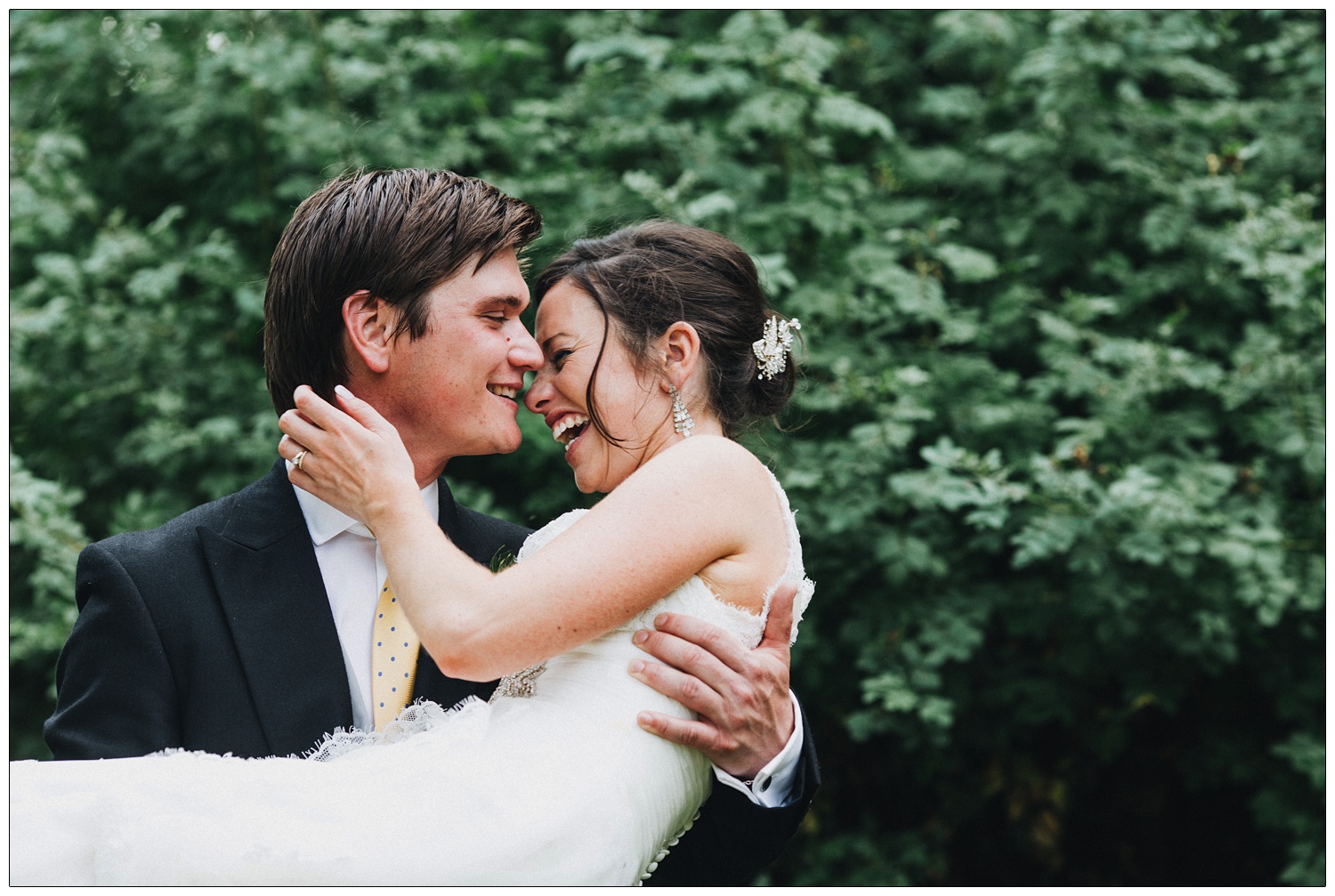 Groom is carrying his wife who is laughing.