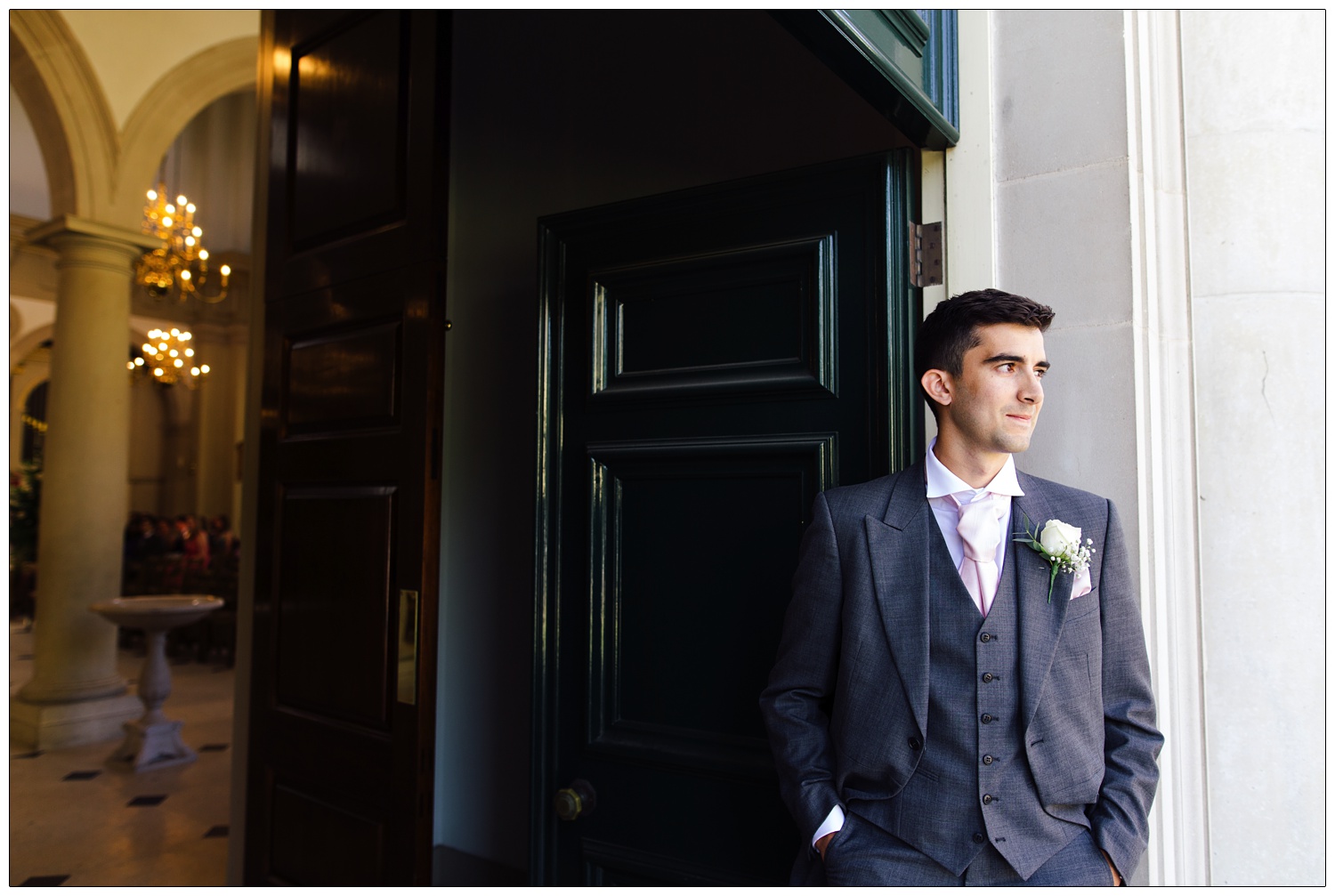 A groomsman is wearing a grey suit in the doorway of Brentwood Cathedral.