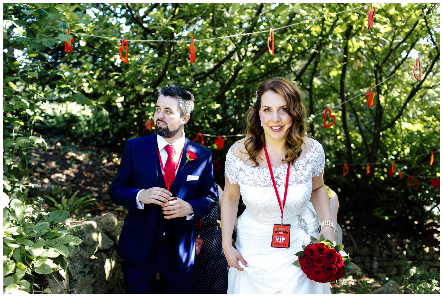 Bride and groom walking up the garden stairs through some trees. The bride is wearing a lace dress and the groom is in a blue suit.