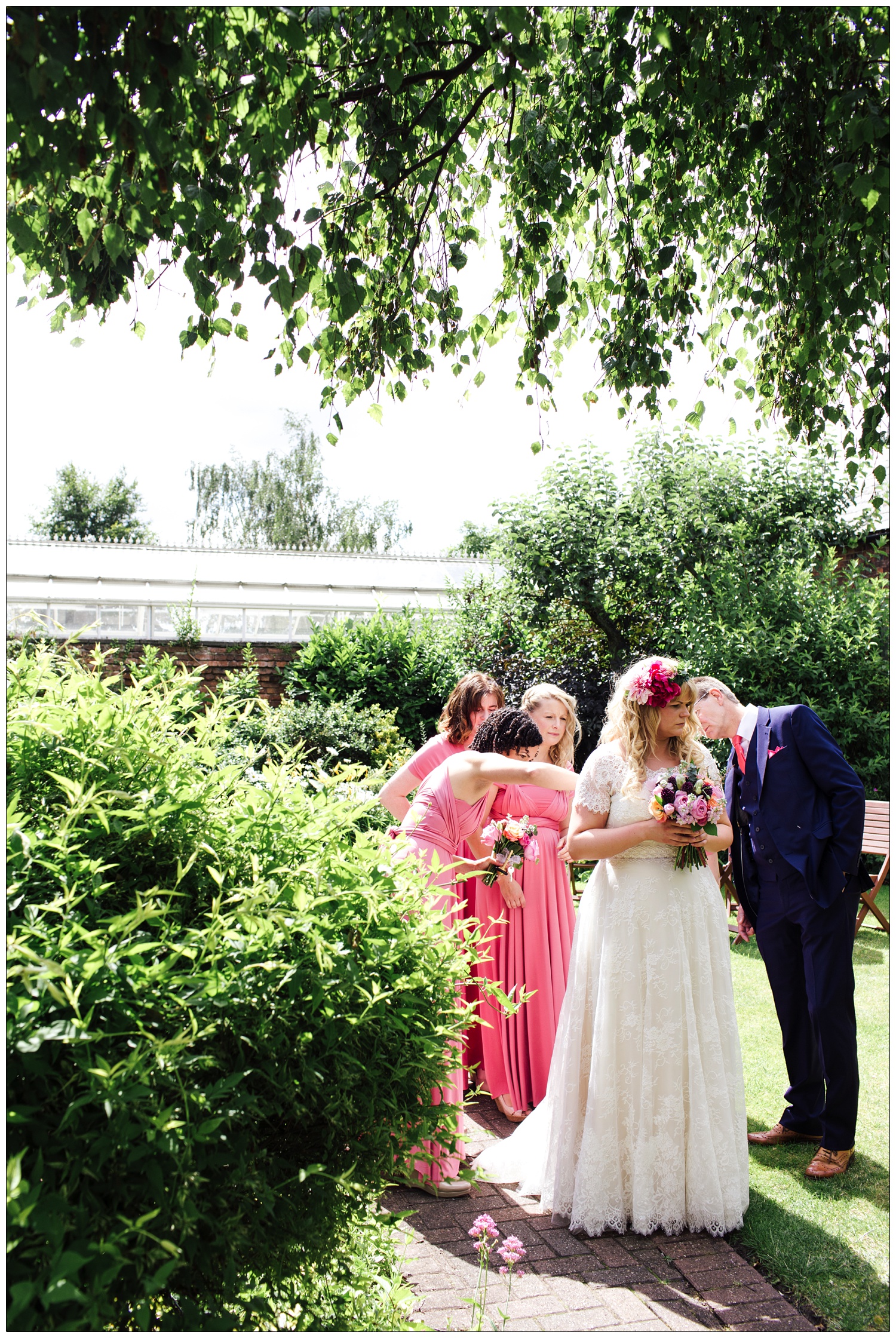 Bride in a garden with her bridesmaids and dad.