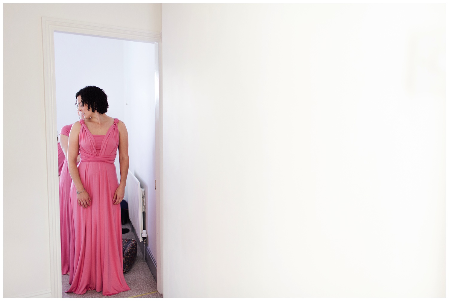 Bridesmaid in a doorway having her pink dress tied up.