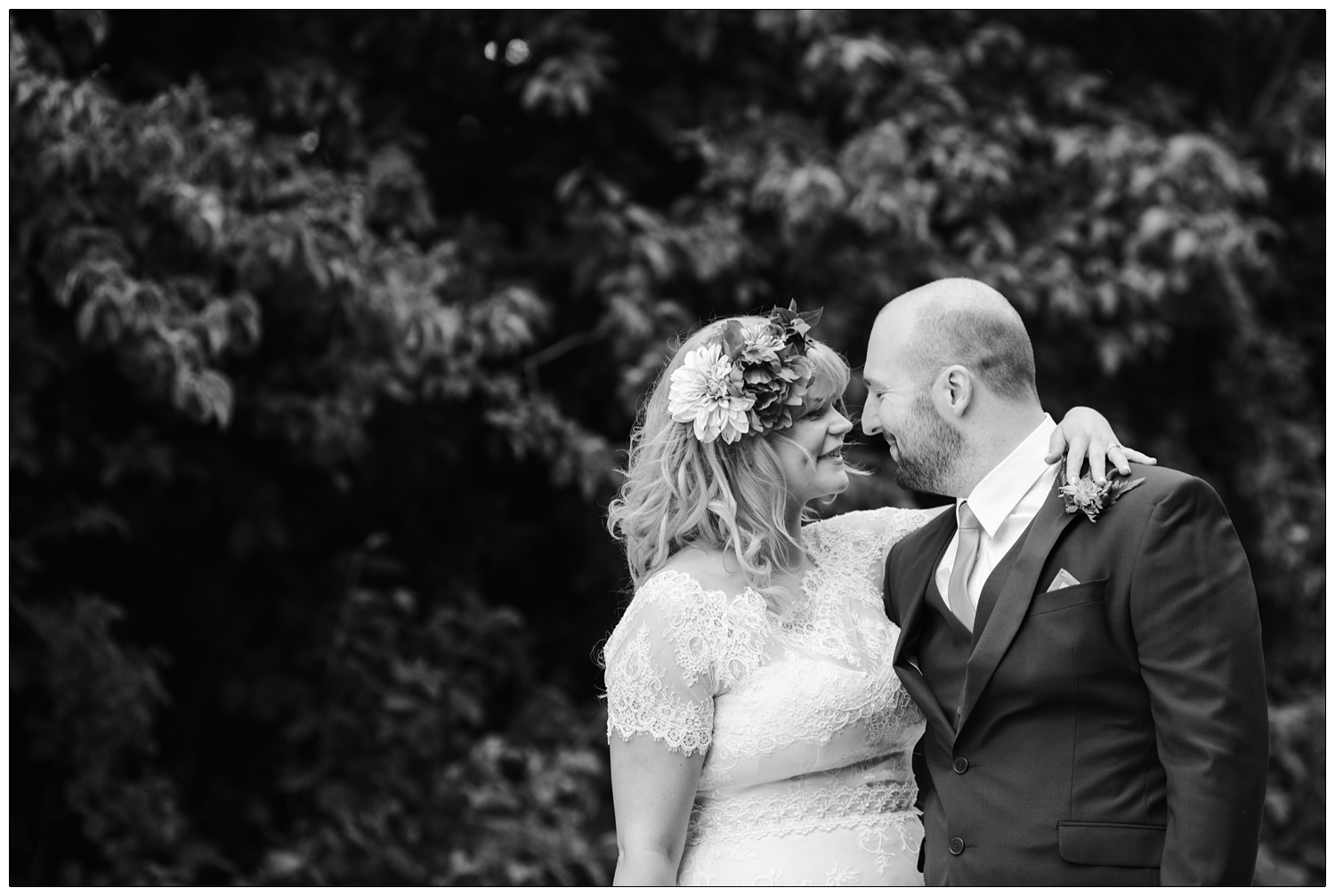 Black and white wedding portrait. Bride has her arm around the groom and is almost kissing.
