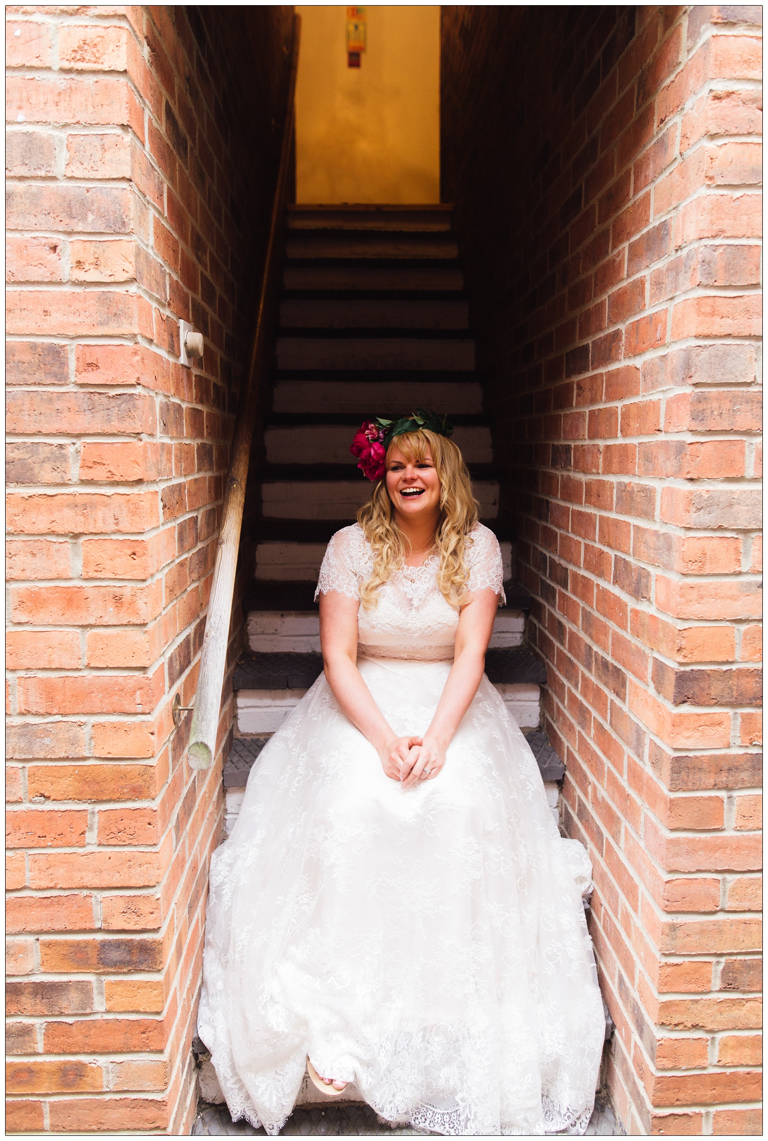 A bride sits on steps with brick walls at the sides. She is laughing and has flowers in her hair. At The Cottage Hotel Ruddington.