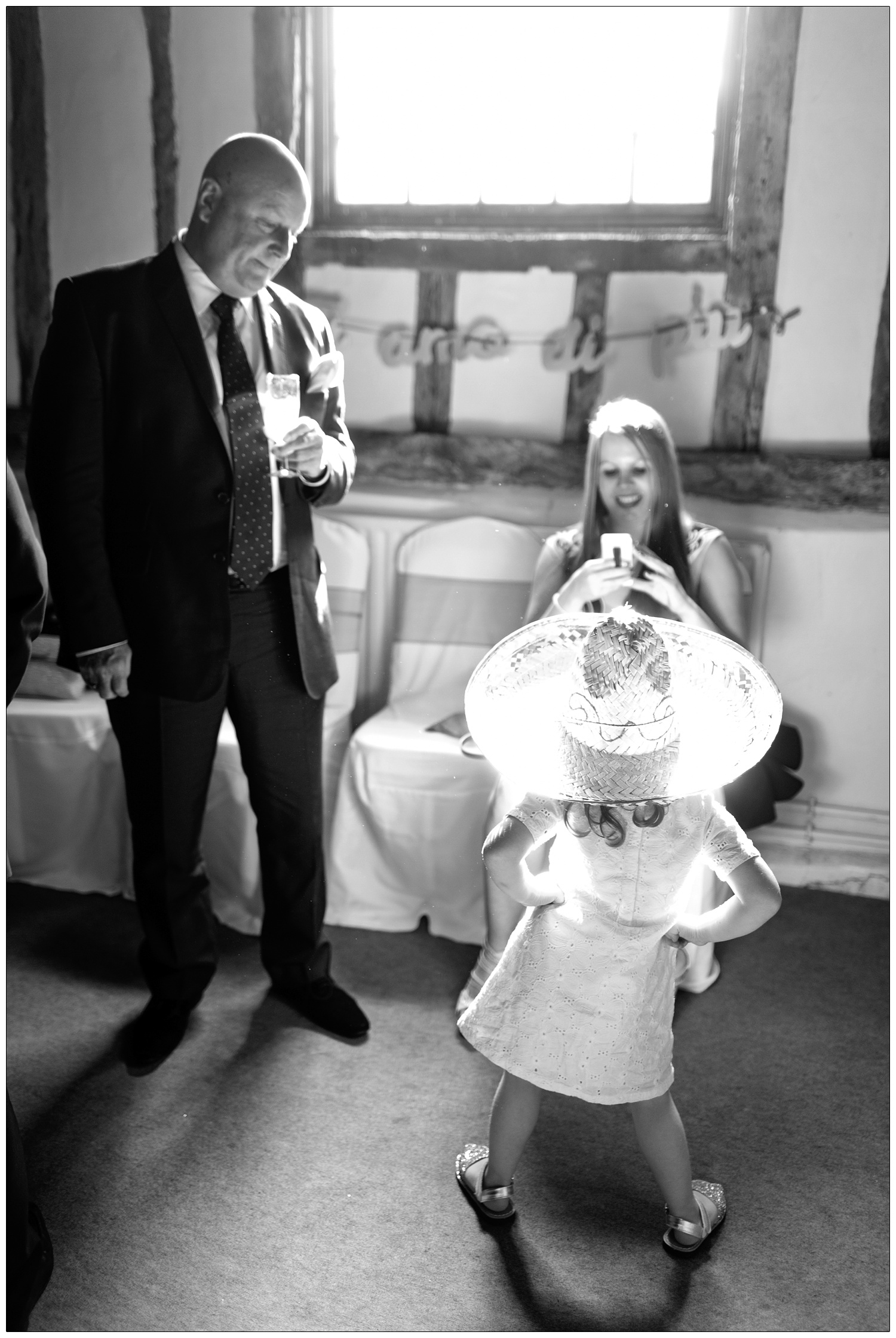 A girl trying on a big hat from a dressing up box. A woman takes a phone with her phone.