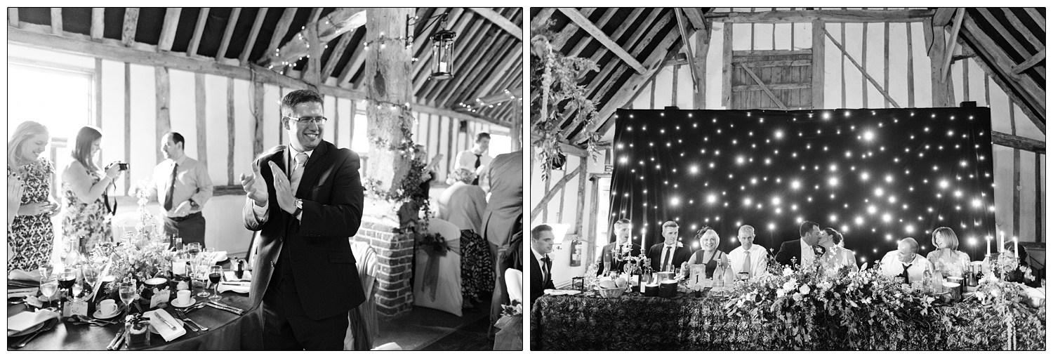 Bride and groom sit at the top table and kiss, there is a wall of lights behind them.