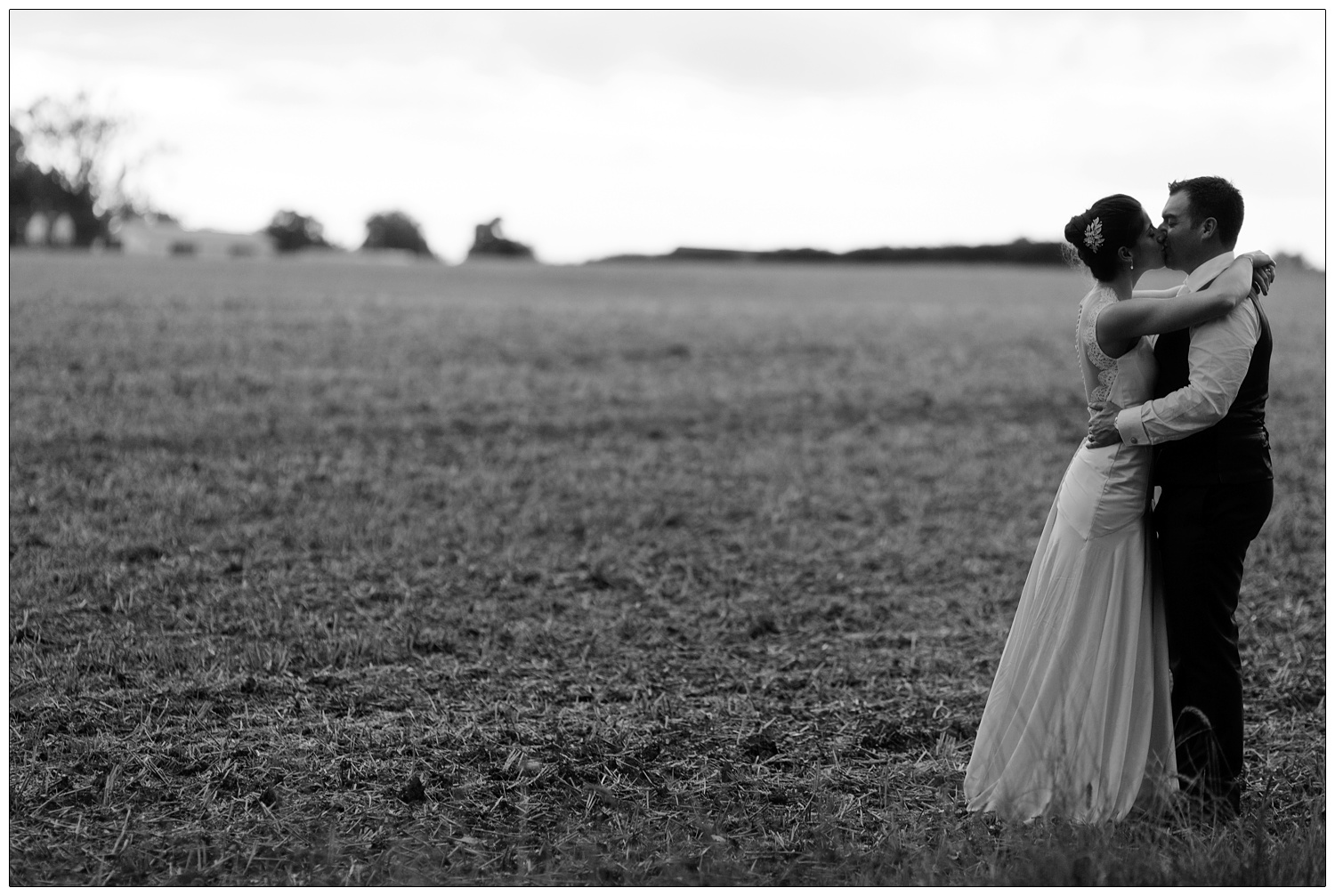 Bride and groom are kissing in a field.