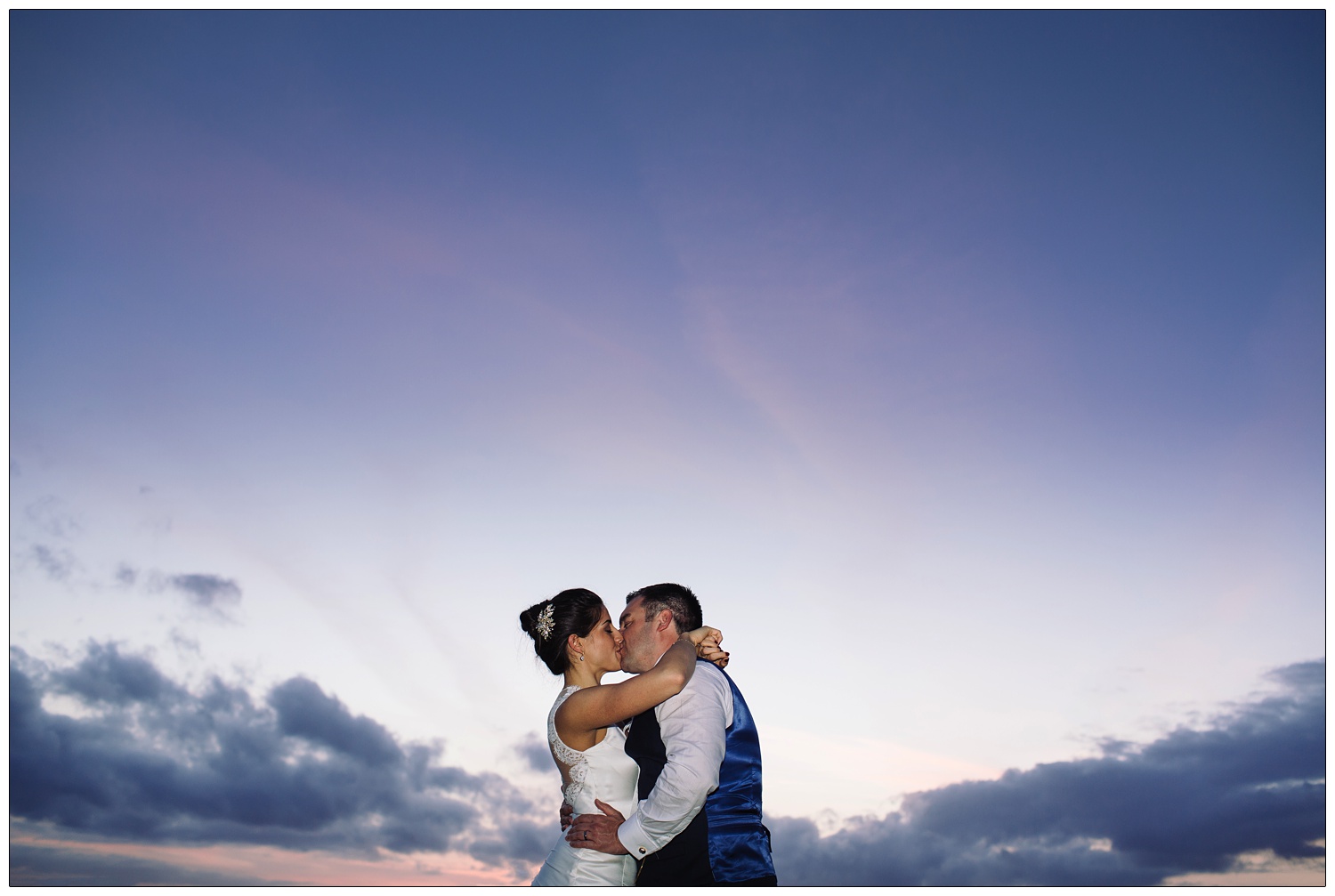 Bride and groom iss outside as the sun is setting. There are a few clouds on the horizon.