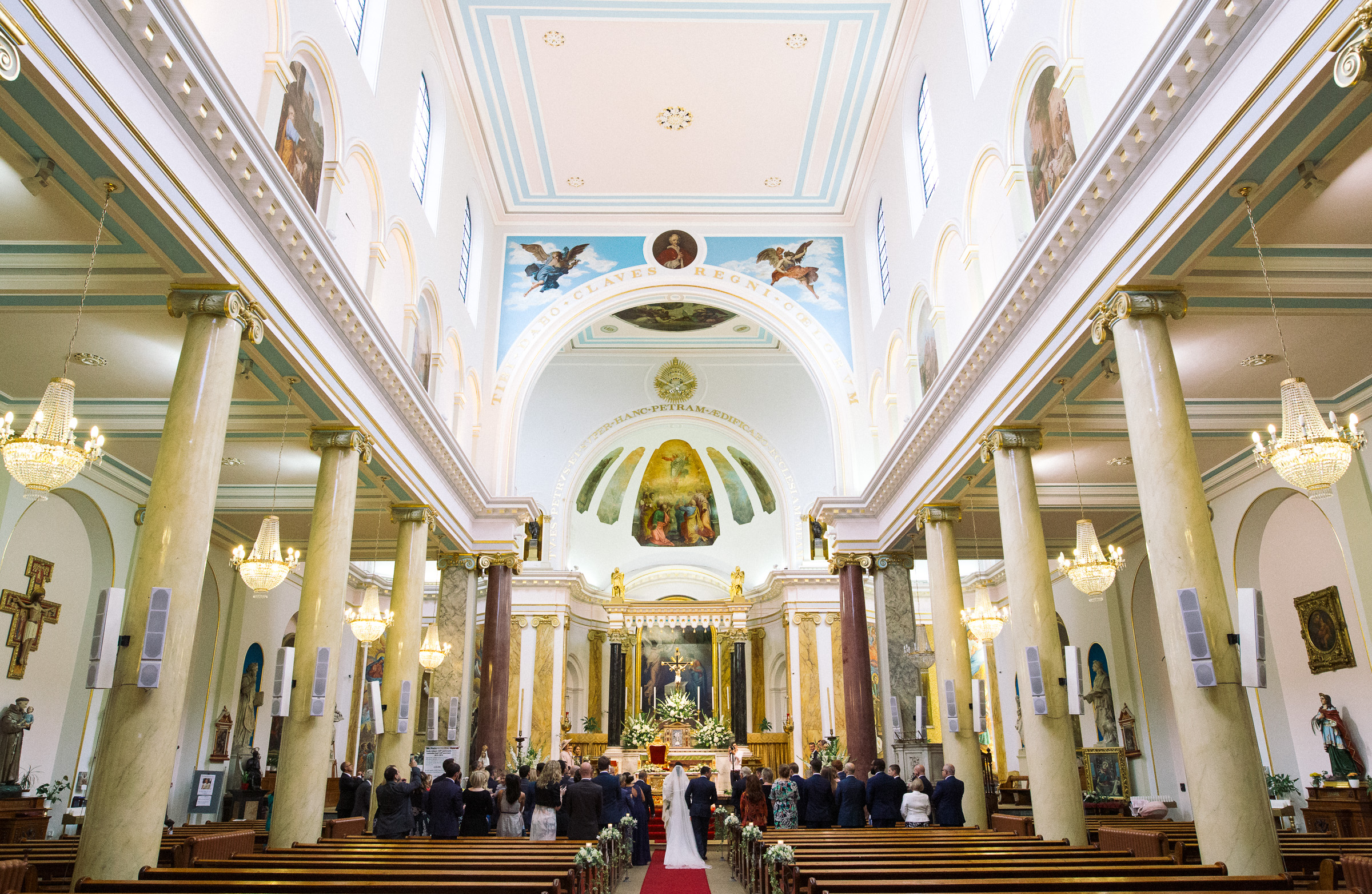 The bride has walked up aisle with her father. The view from behind as the veil trails on the red carpet. A wedding in St. Peter's Italian Church in Clerkenwell.