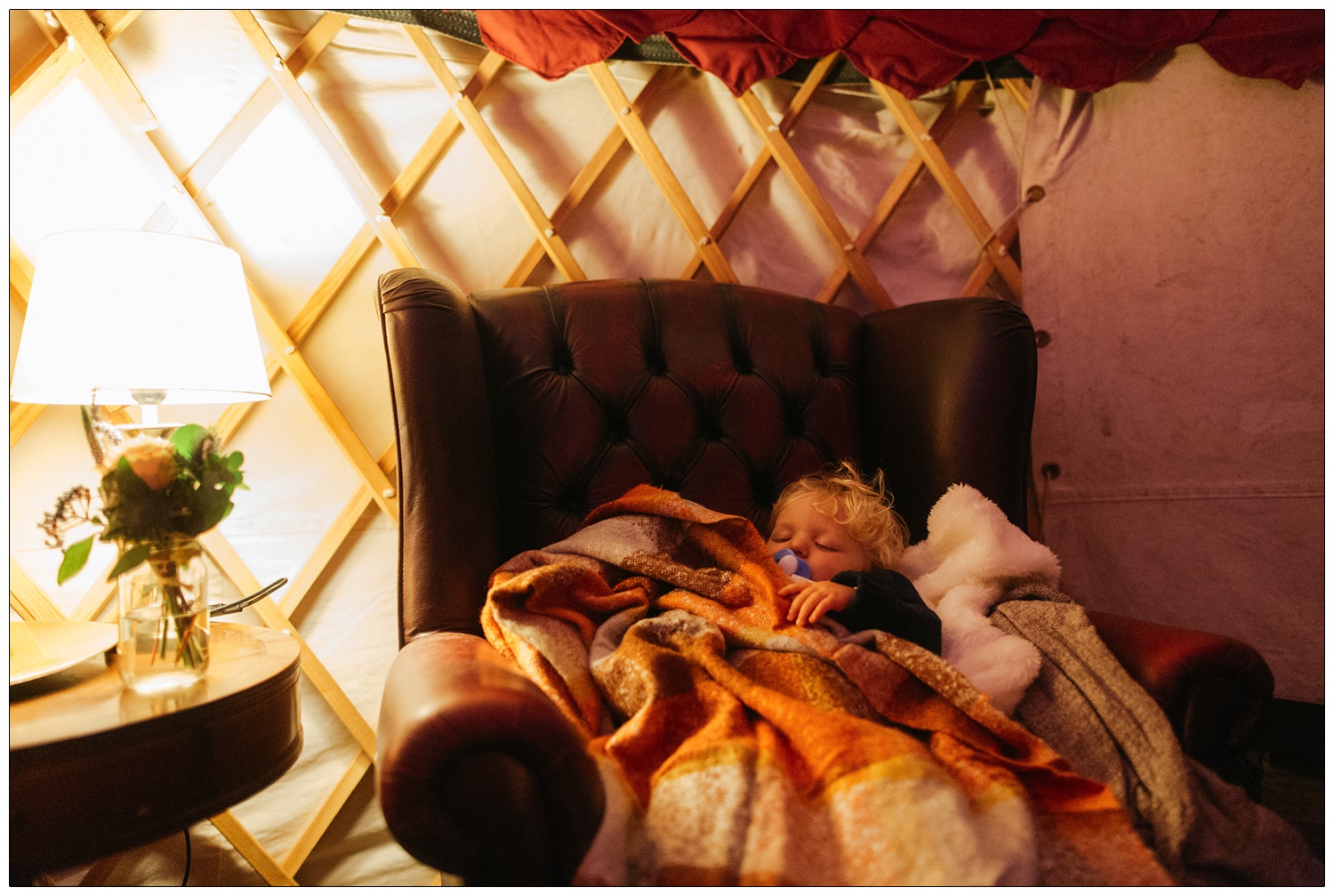 A toddler boy with blonde hair is asleep in an armchair at a wedding.