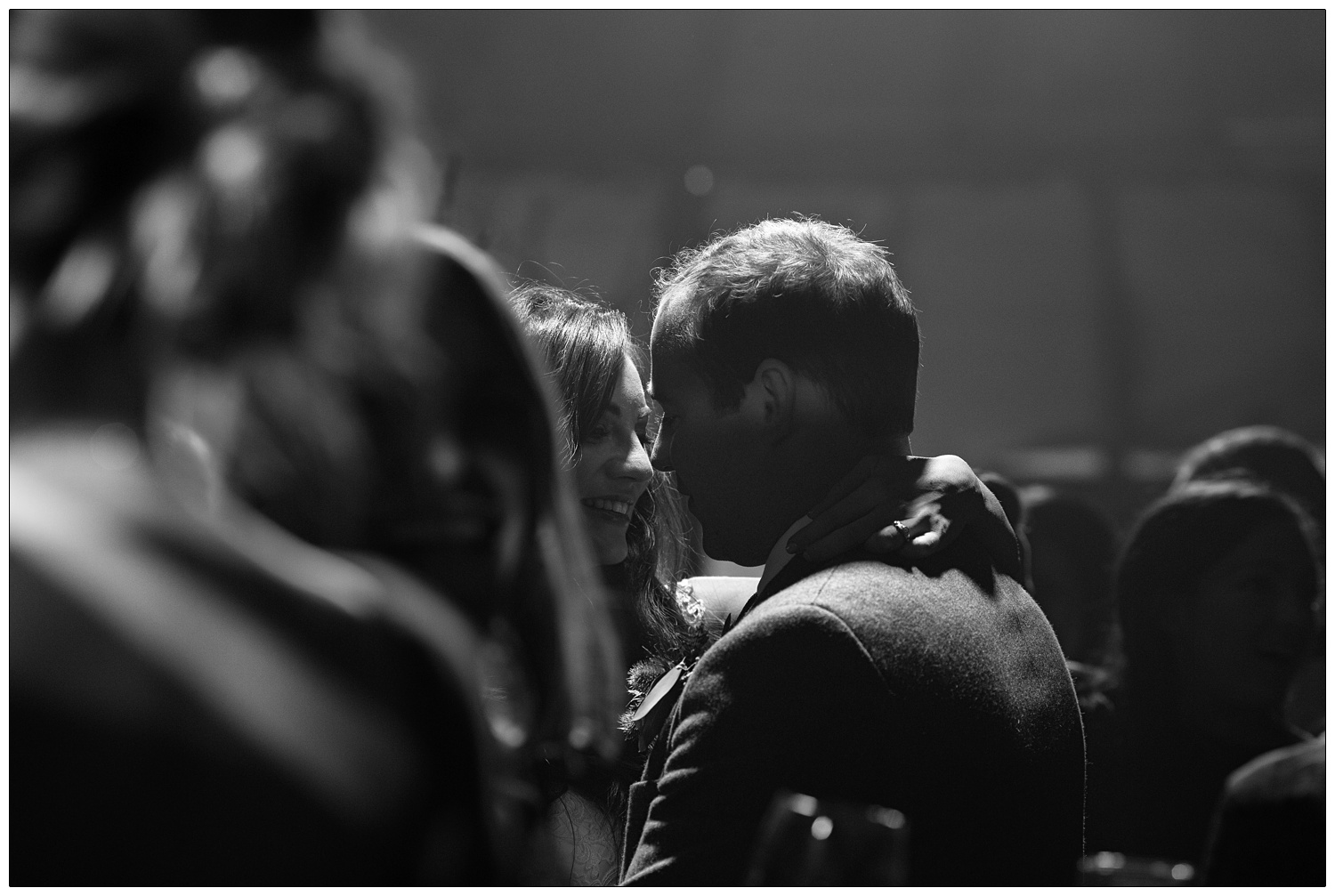 A black and white candid photograph of the bride and groom dancing together. Surrounded by people but they appear to only notice each other.