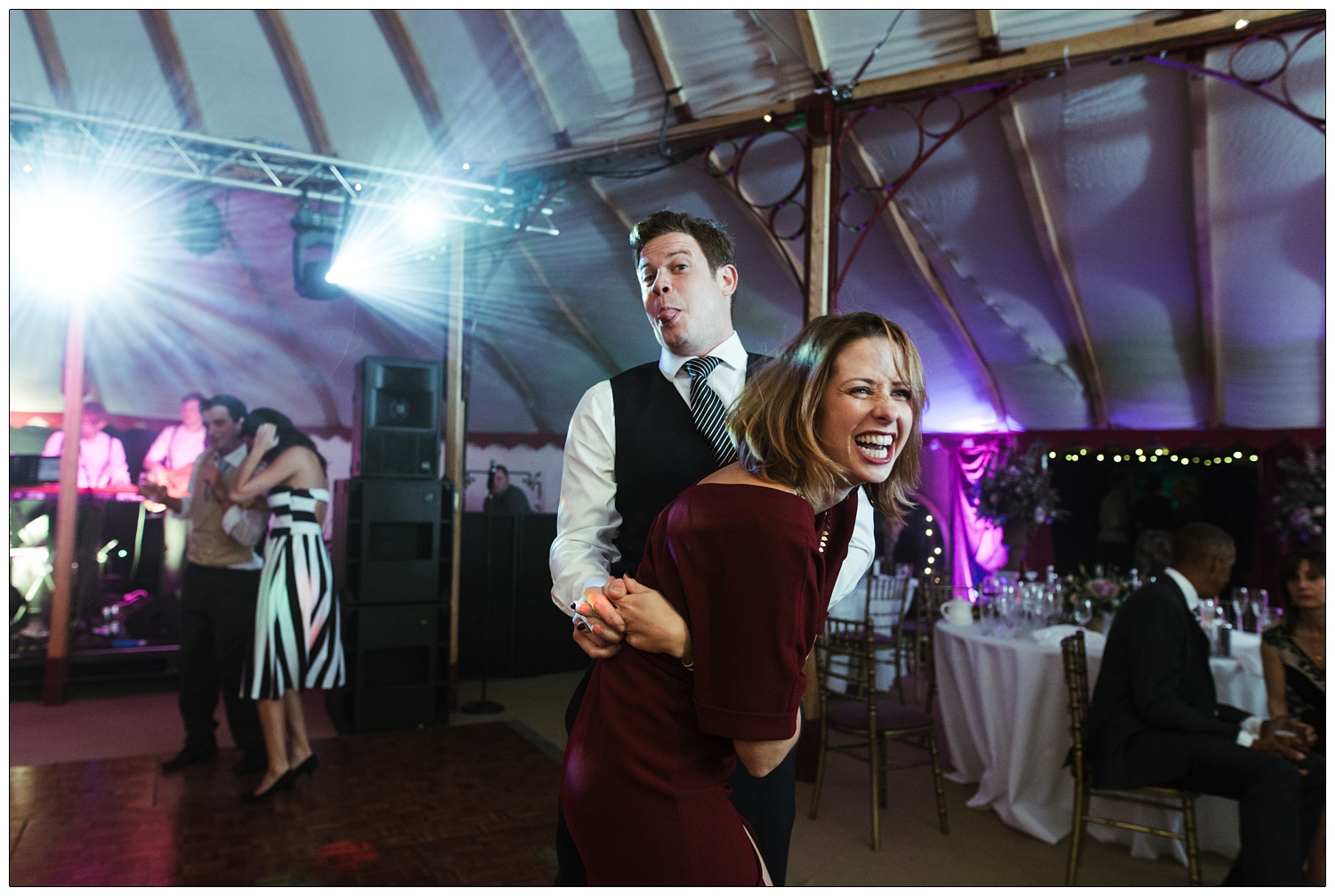 A man and a woman are dancing and the man is sticking out his tongue at the camera.