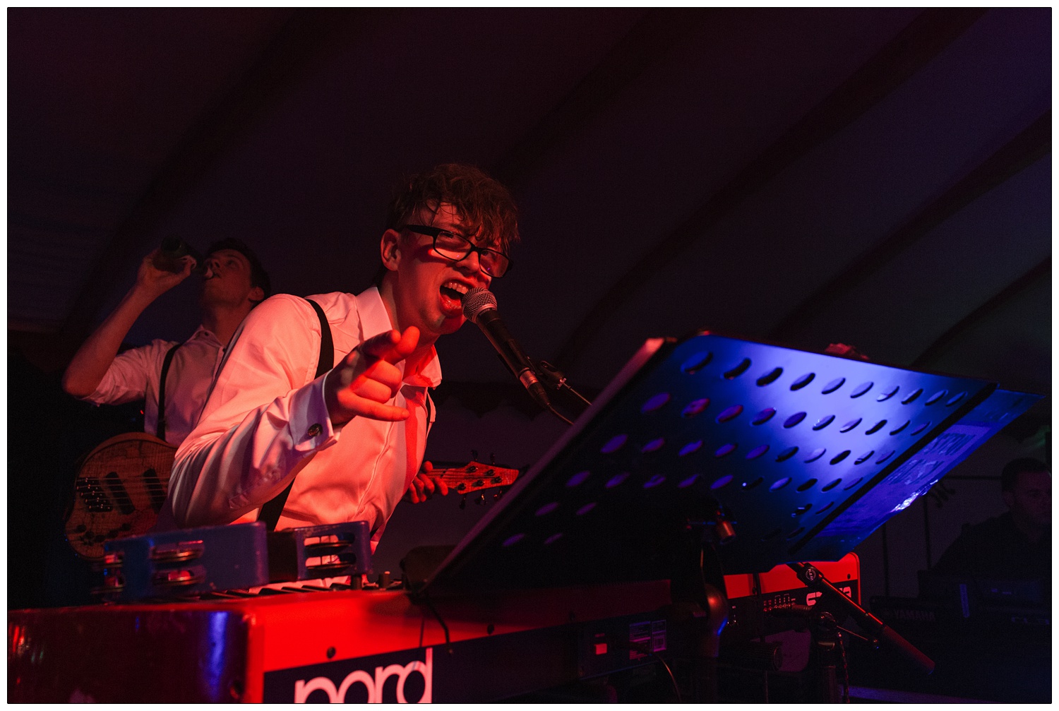 Alex of Winston and the Lads is playing his Nord keyboard and pointing at the photographer while he sings.