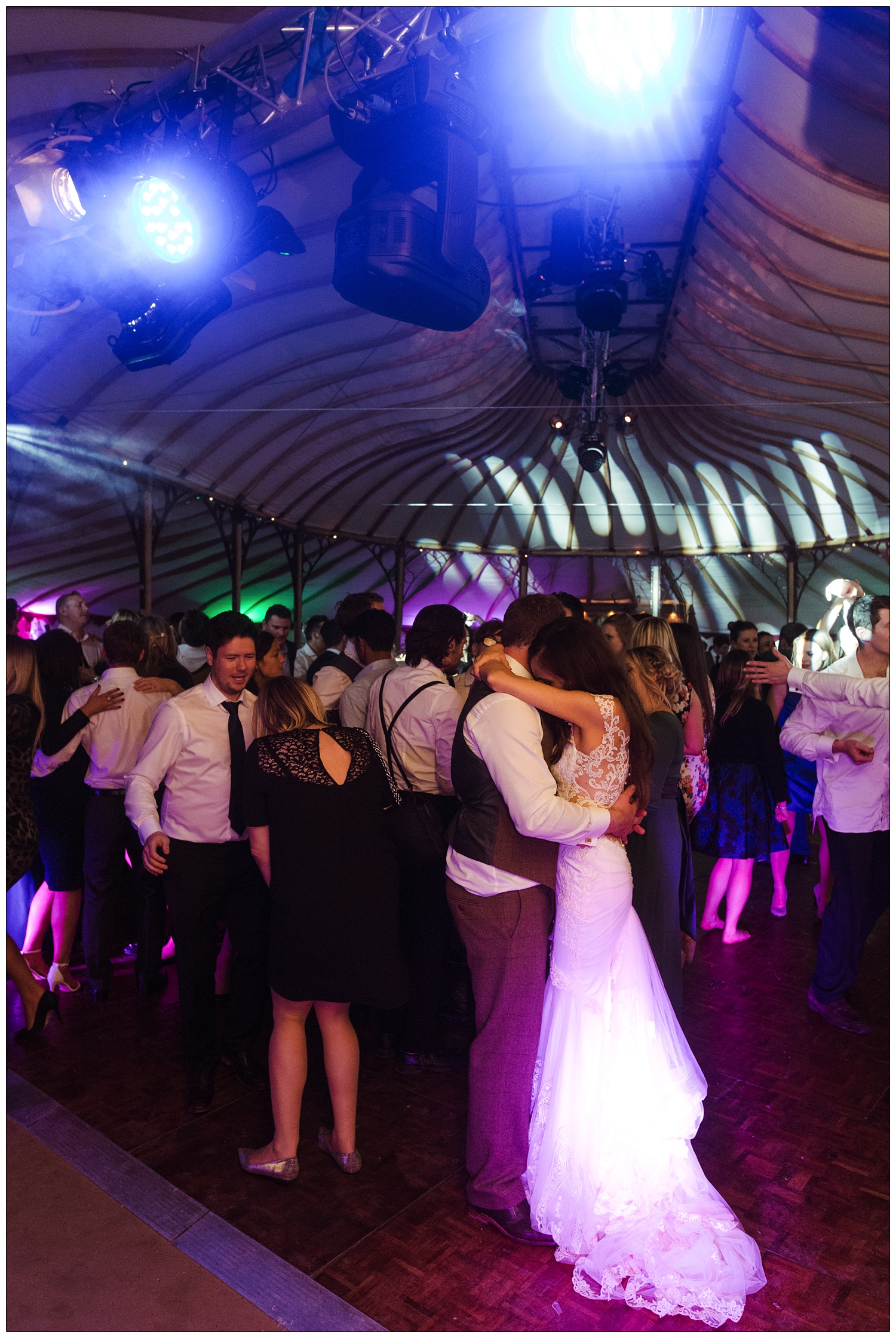 Bride and groom hold each other on the dancefloor whilst surrounded by people.