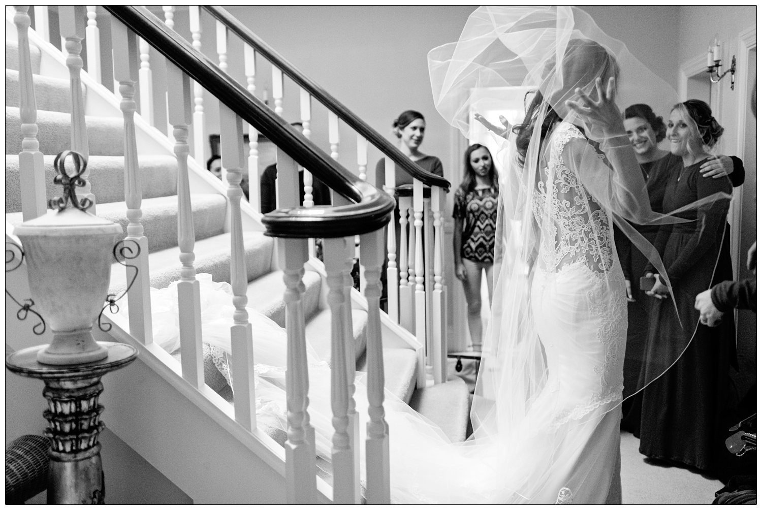 Bride flips off her veil as she walks down the stairs at home. Her bridesmaid smile.