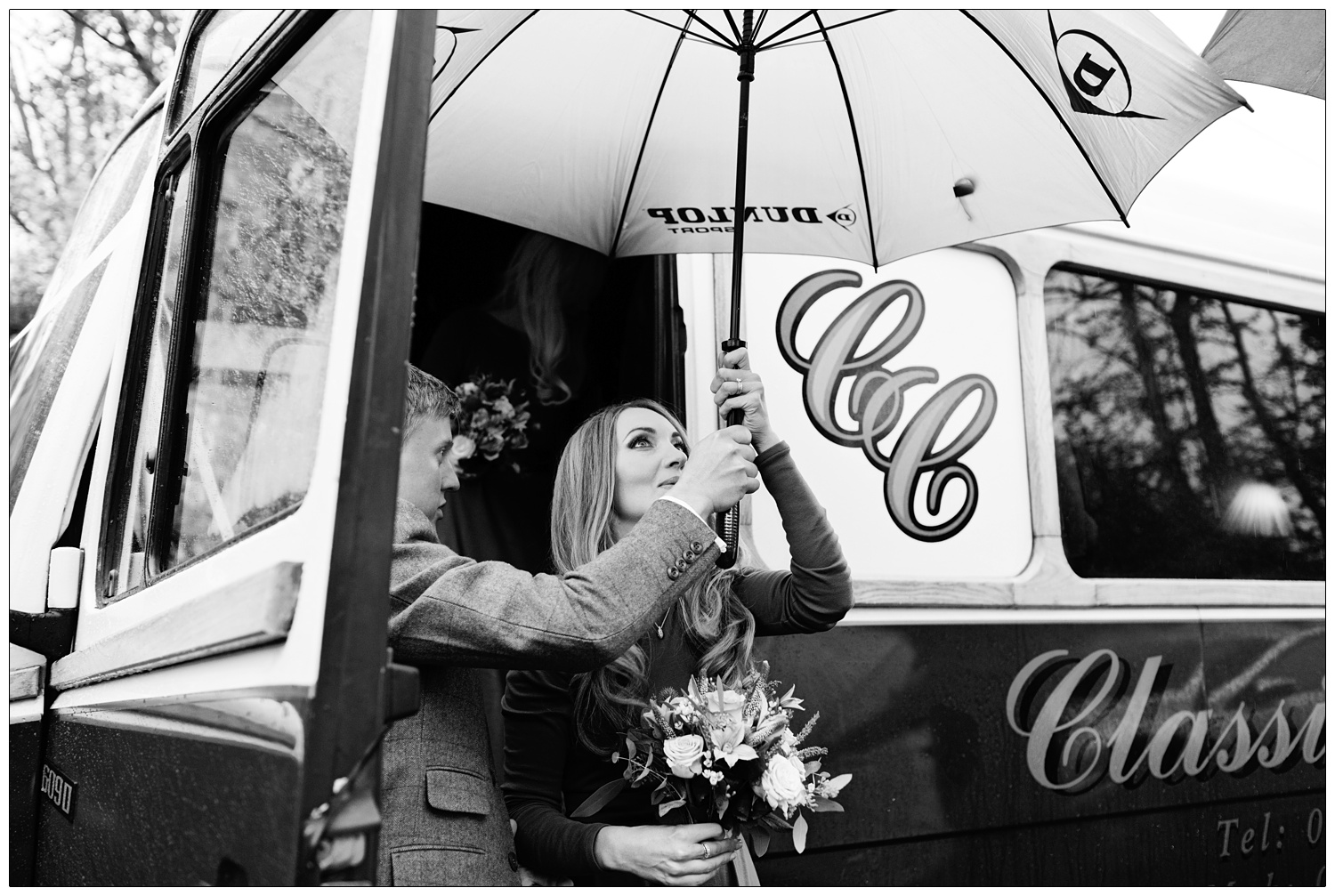 A bridesmaid steps off a coach and an usher hands her an umbrella.