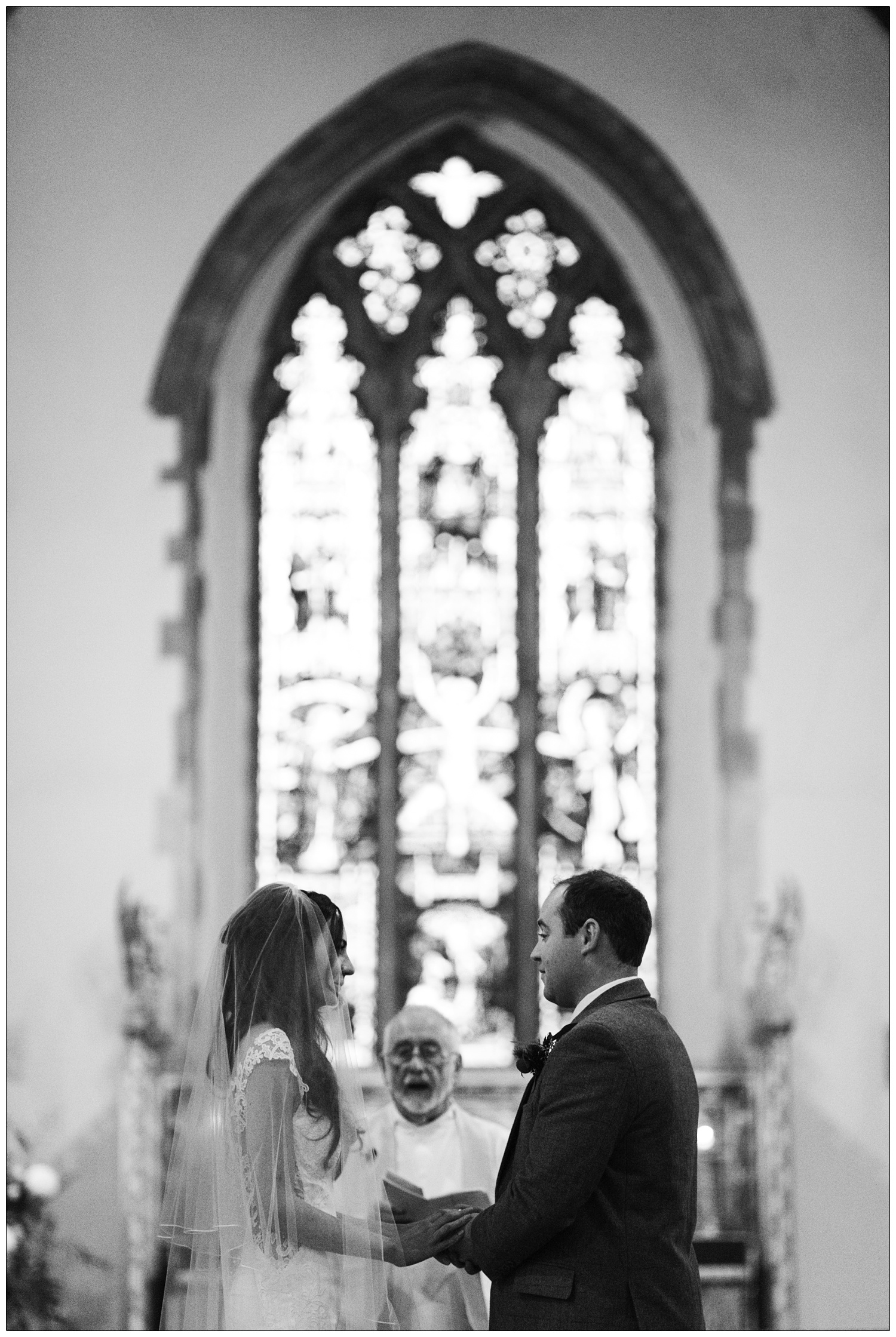 A couple hold hands in the All Saints Church in Purleigh. The vicar and window are in the background