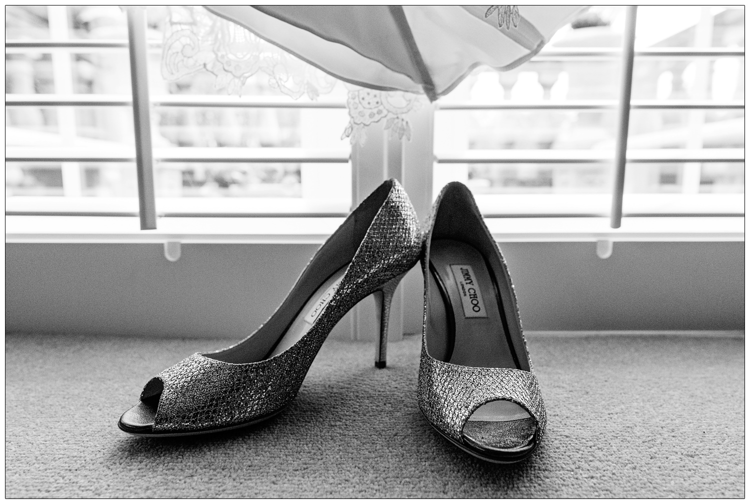 Shiny Jimmy Choo shoes place under a wedding dress. There are window shutters behind them.