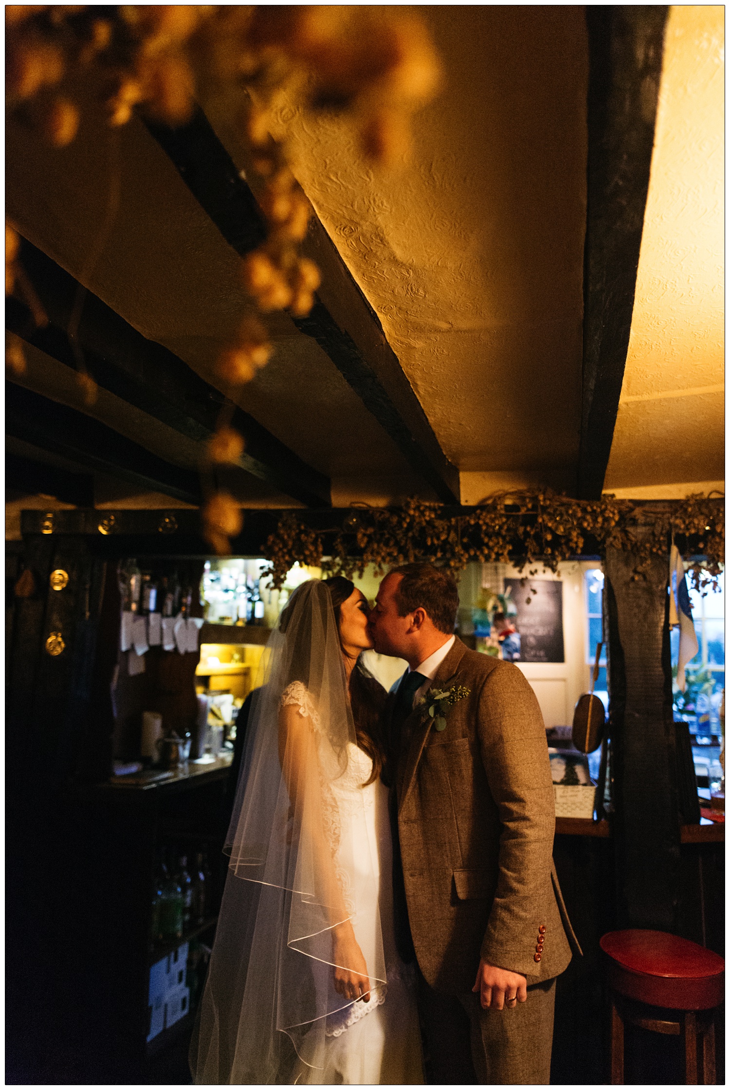 Inside the Purleigh Bell the bride and groom kiss. There are beams on the ceiling.